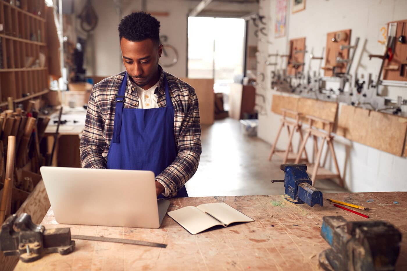 Male Craftsman In Carpentry Workshop For Bamboo Bicycles Doing Accounts On Laptop