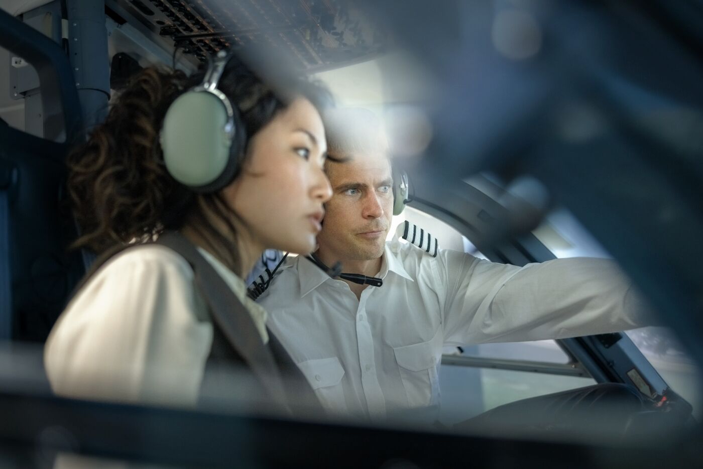 Pilot explaining how a flight simulator works to a female student during a training session. Male pilot talking with woman trainee pilot sitting inside a flight simulator.