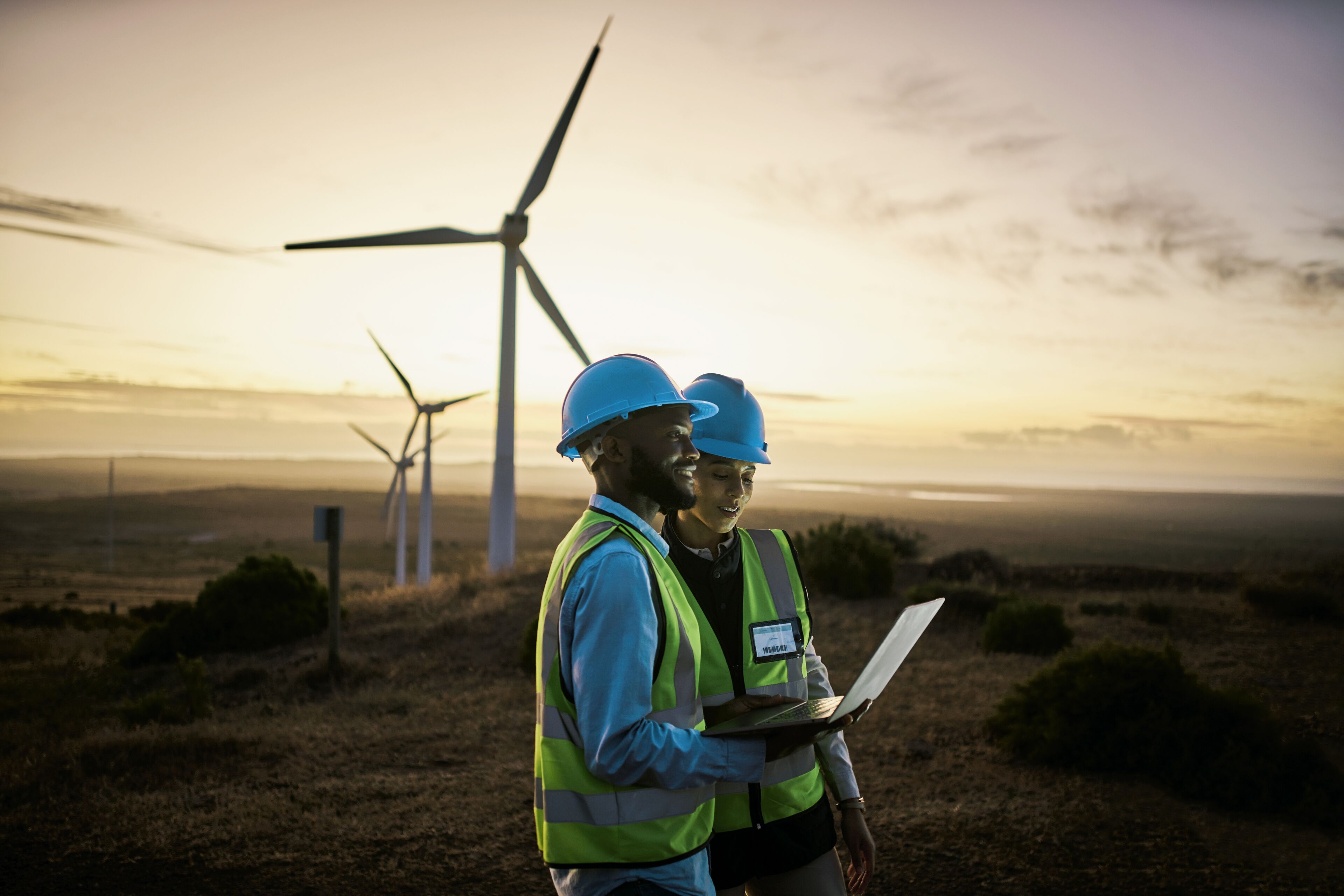 Laptop, farm and engineer team together at night for renewable energy, power and wind turbine. Electrician or technician man and woman in nature for electricity, eco and green environment maintenance