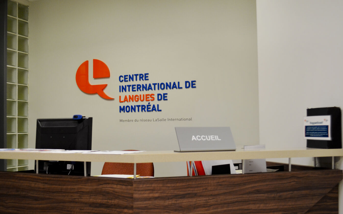 The reception area of the Centre International de Langues de Montréal features a sleek wooden desk and prominent signage with the center’s logo. The minimalist decor and professional setup provide a welcoming environment for visitors.