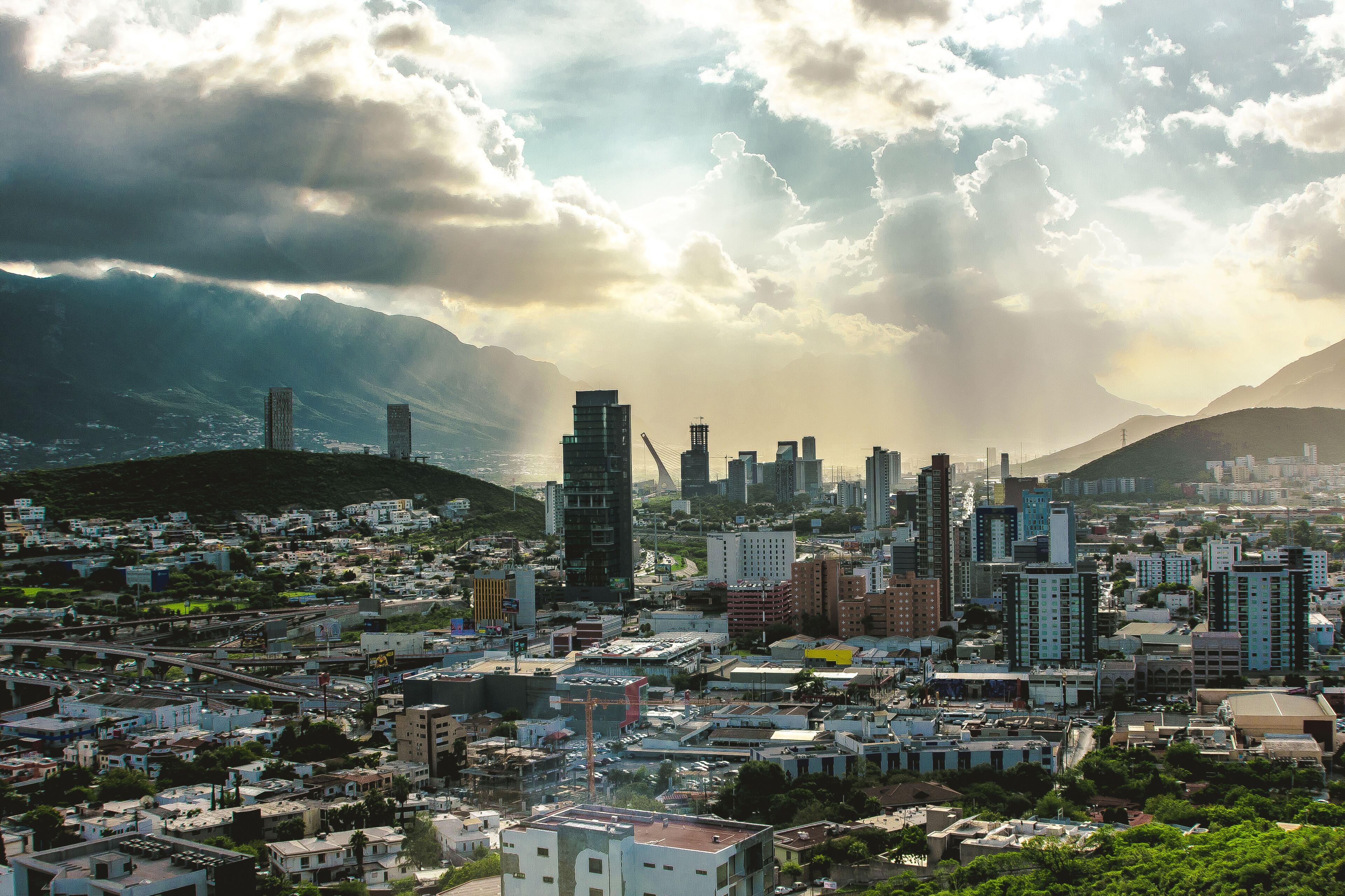 Panoramic view of the city of Monterrey with a view of the mountains and the cloudy sky letting in the sun's rays.