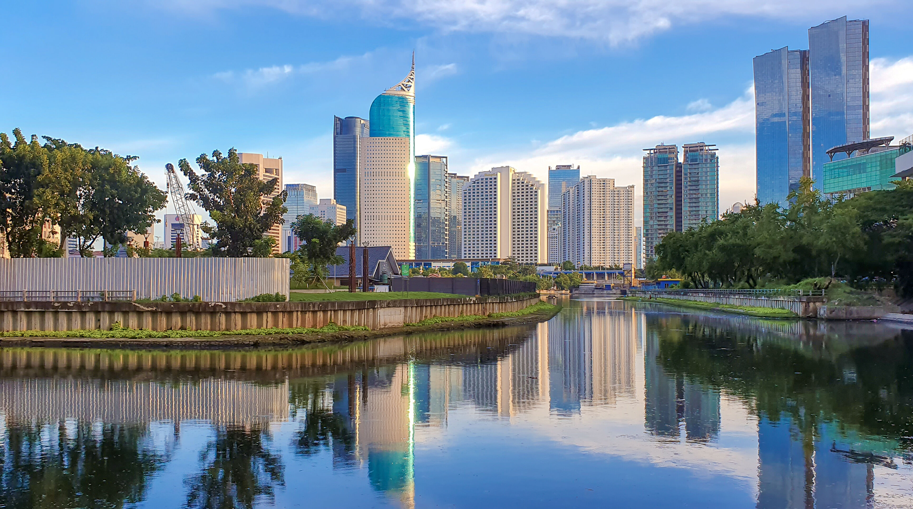 View of Jakarta, capital of Indonesia, at blue hour, a calm river in the foreground with iconic buildings on the horizon.