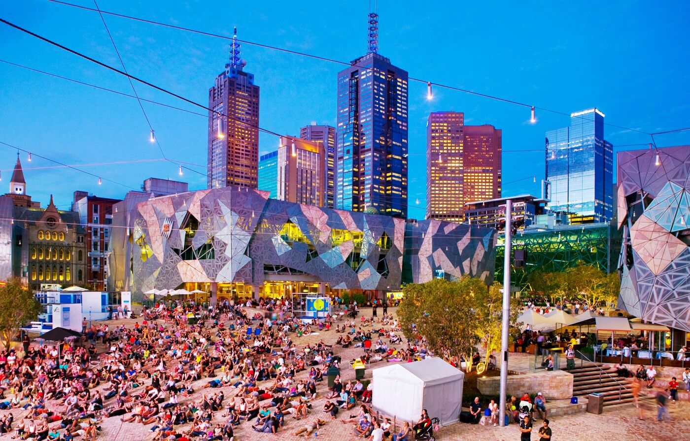 Gathering of people sitting and lying in Federation Square illuminated at dusk. Australia, Victoria, Melbourne. 