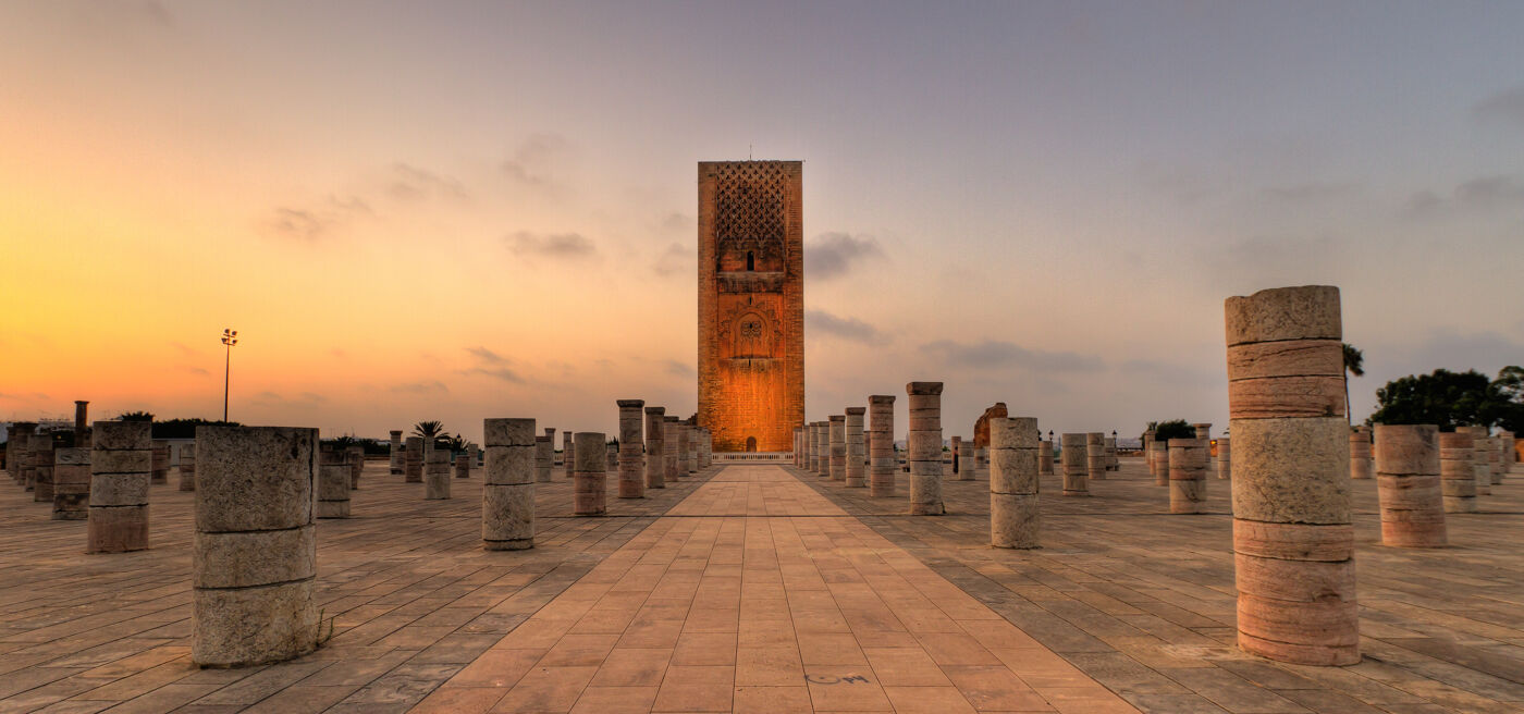 A serene sunset bathes Hassan Tower and the remnants of columns in a warm glow, in Rabat, Morocco.