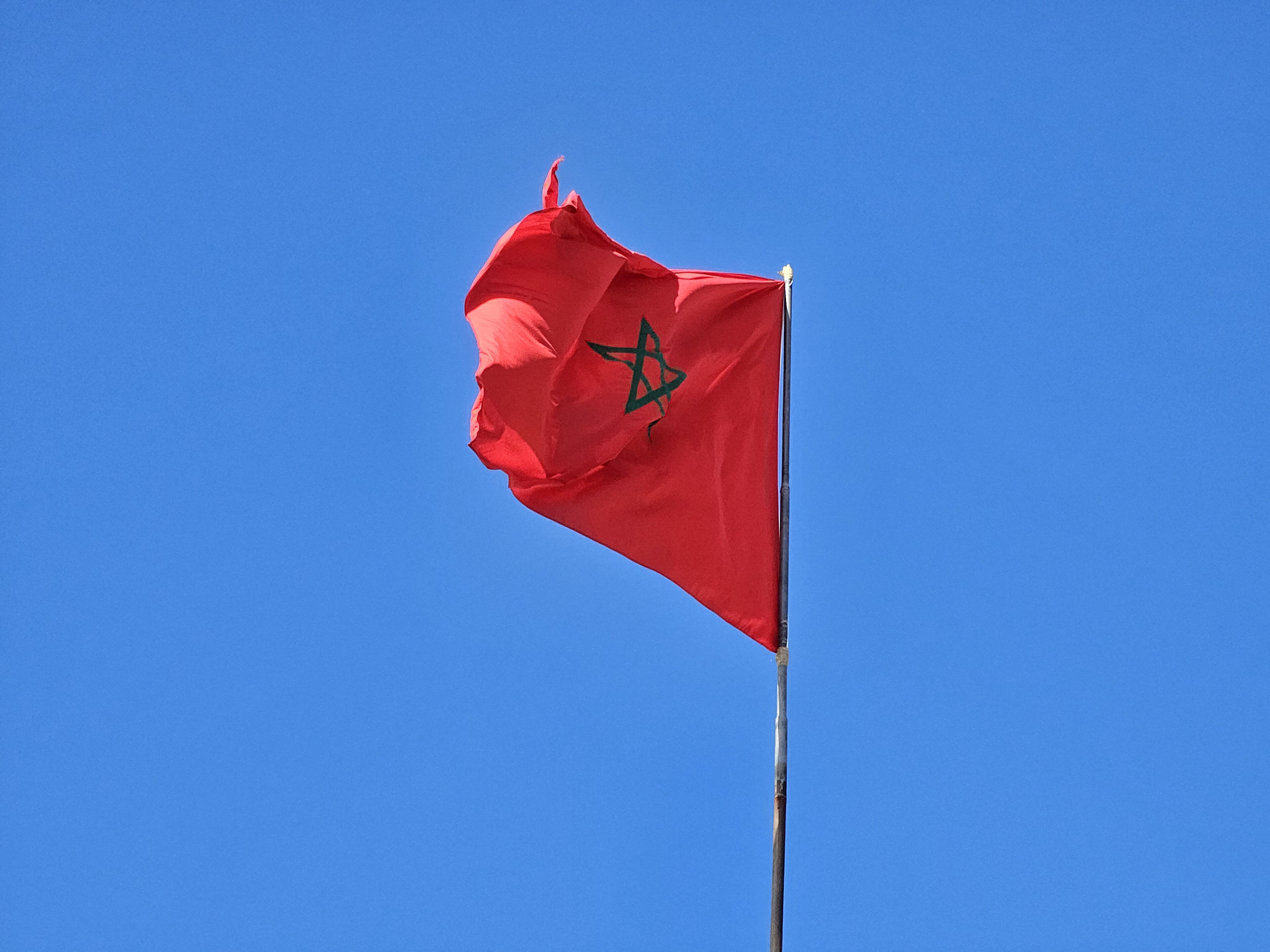 Moroccan flag floating on a blue sky.