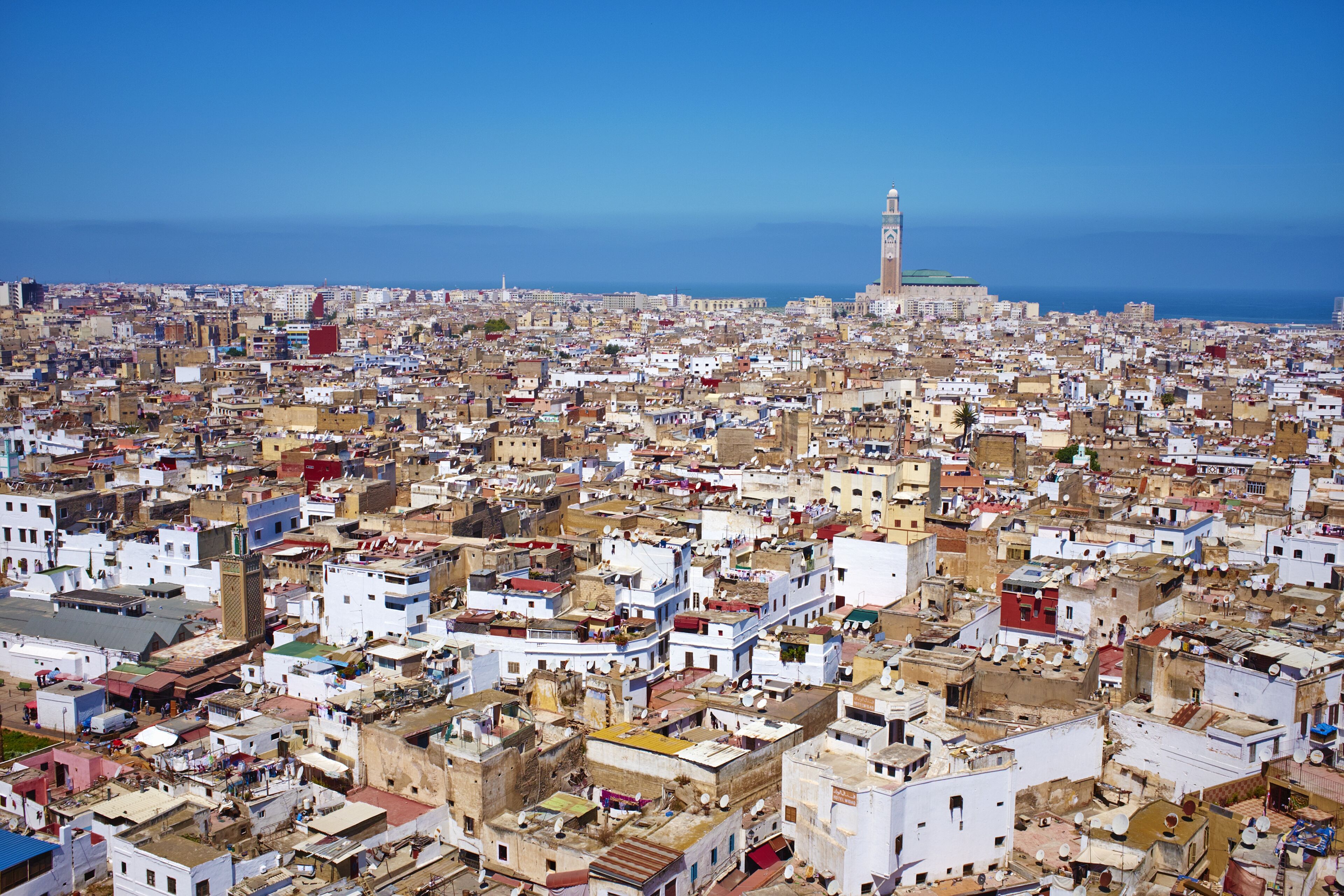 Panoramic view over Casablanca's dense cityscape, with the Hassan II Mosque's minaret standing tall against the blue sea.