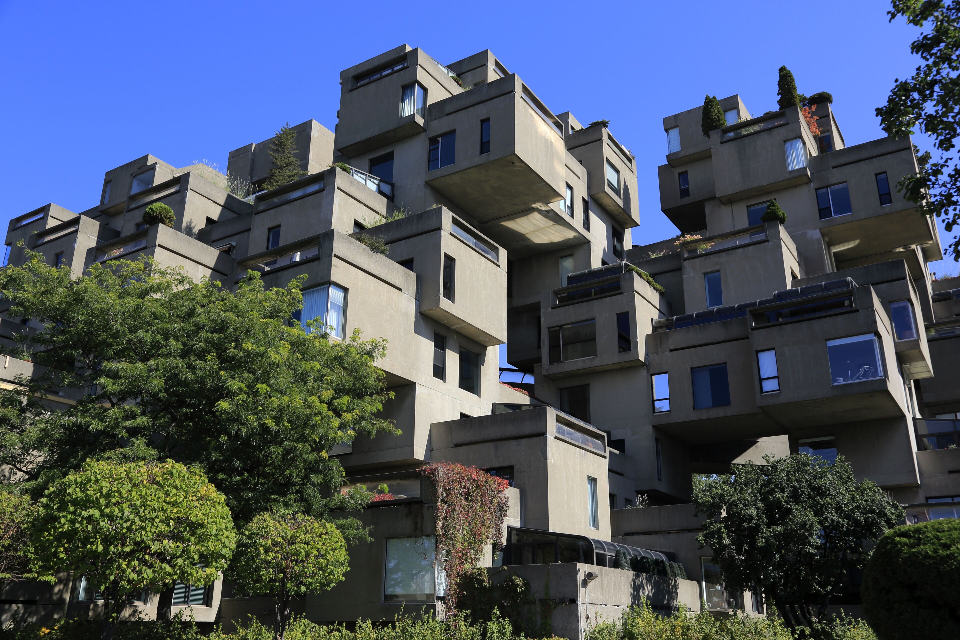 An image featuring a unique modular architectural complex with cubic structures against a clear blue sky, surrounded by lush greenery.