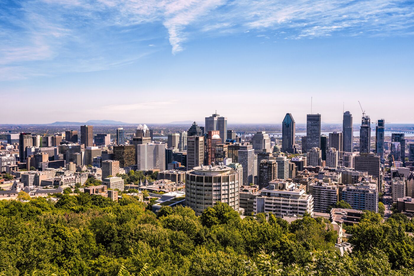 Panoramic view of a city's skyline with a mixture of modern skyscrapers and green areas under a clear sky.