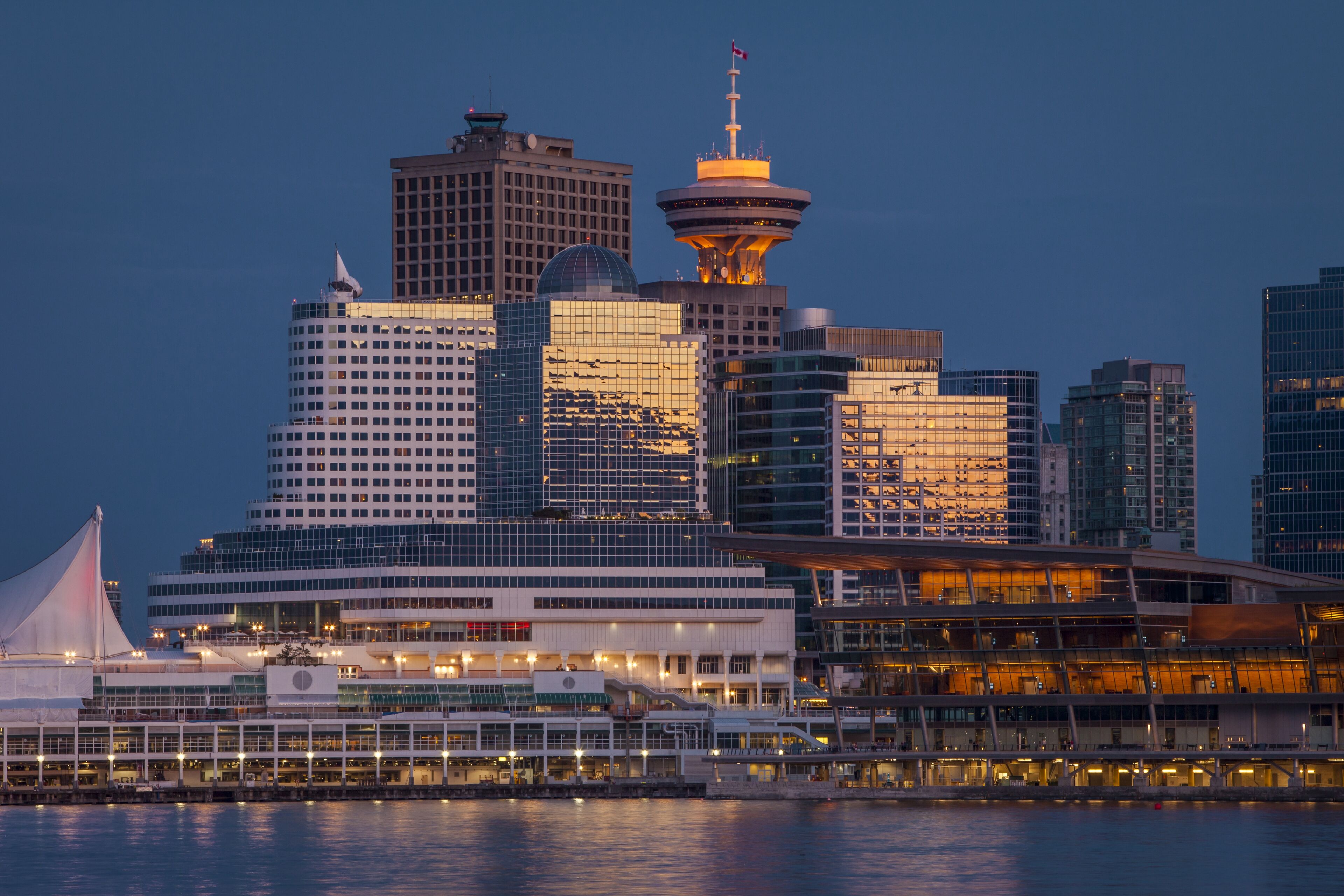The city skyline at twilight, illuminated by lights, with a distinctive tower and reflections on the waterfront buildings.