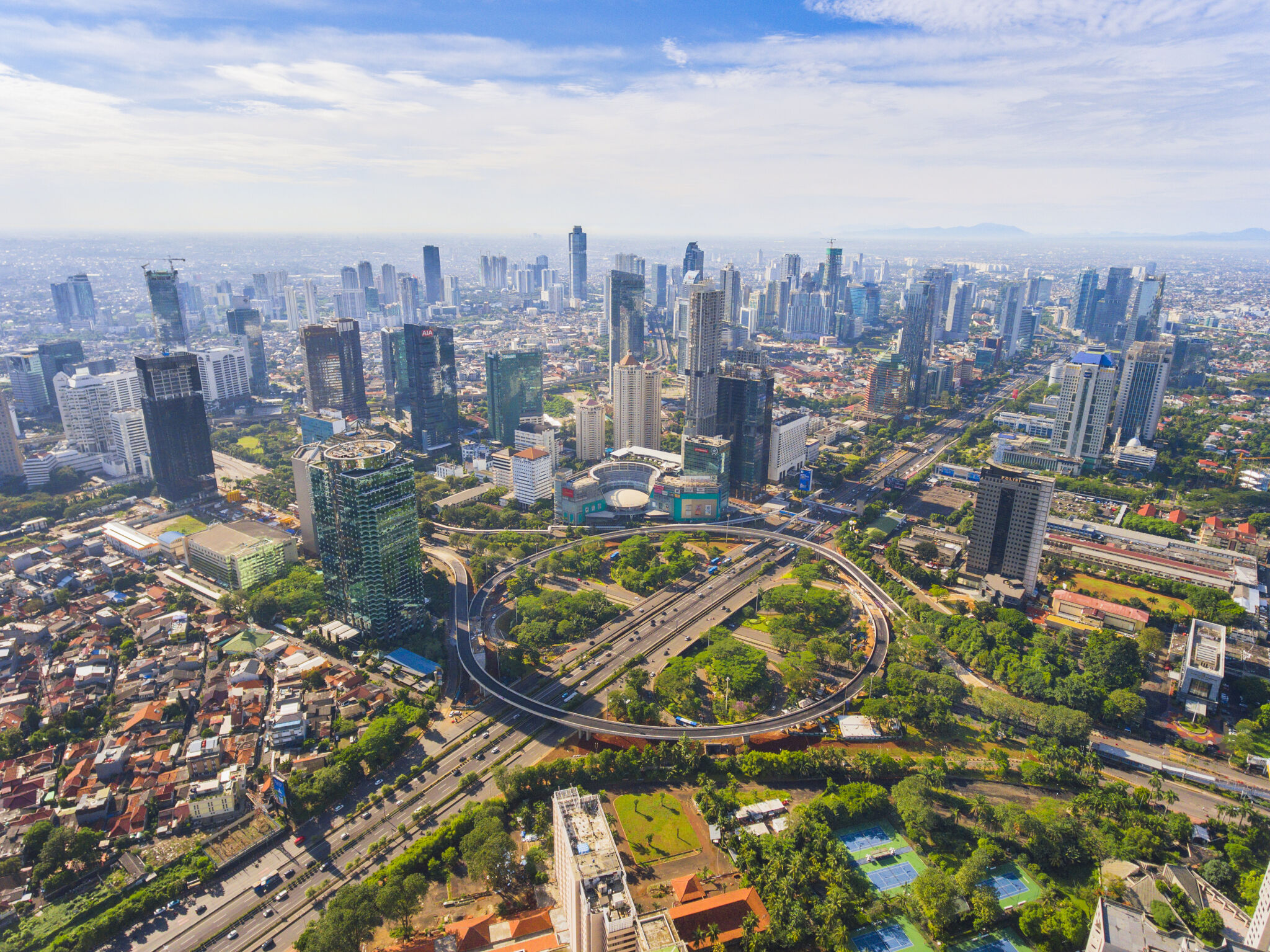 Expansive aerial shot of a modern city's downtown with dense skyscrapers, intertwined roadways, and lush green areas.