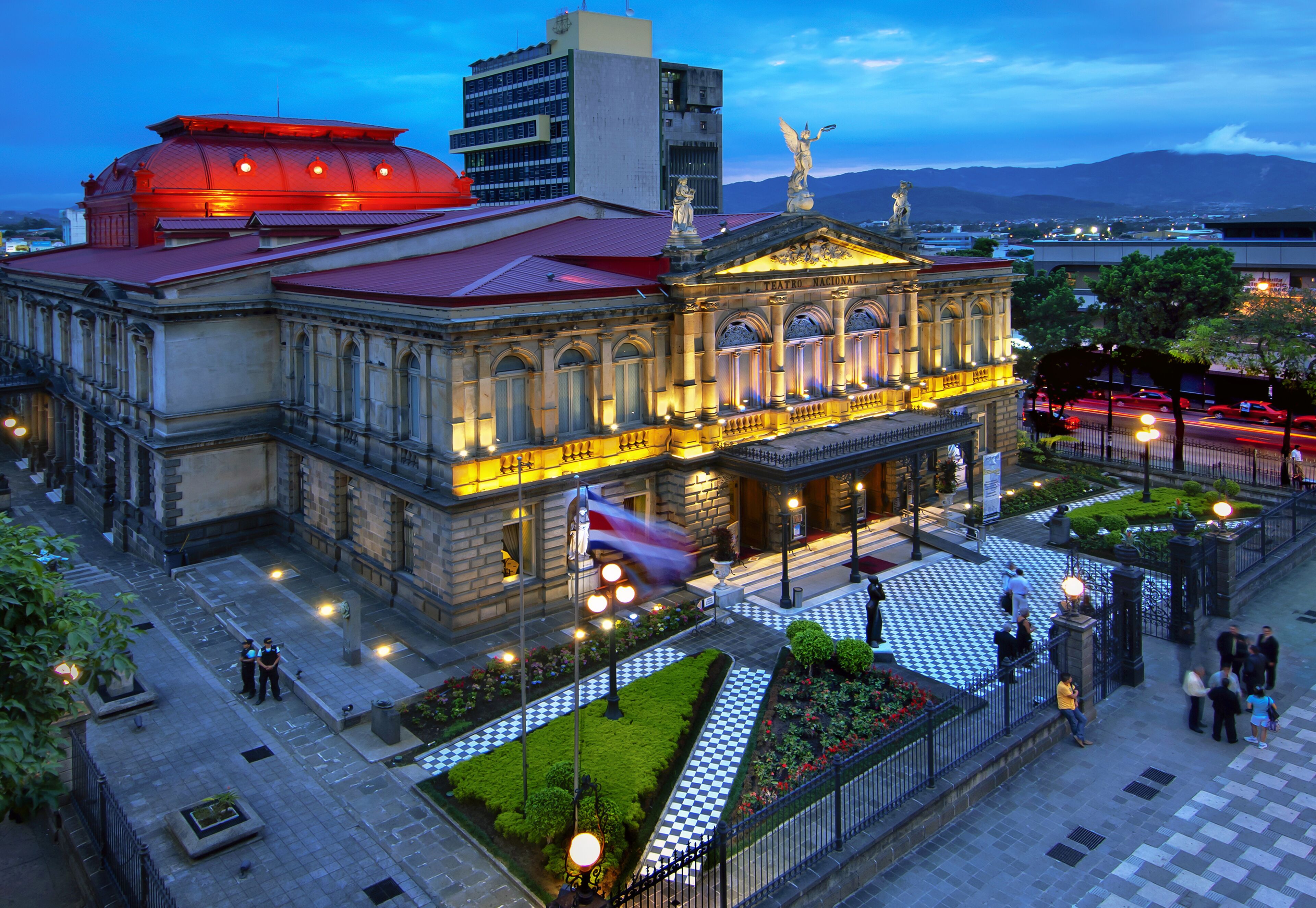 Dusk sets on an ornate historical building with a lit dome, glowing windows, and a bustling foreground.