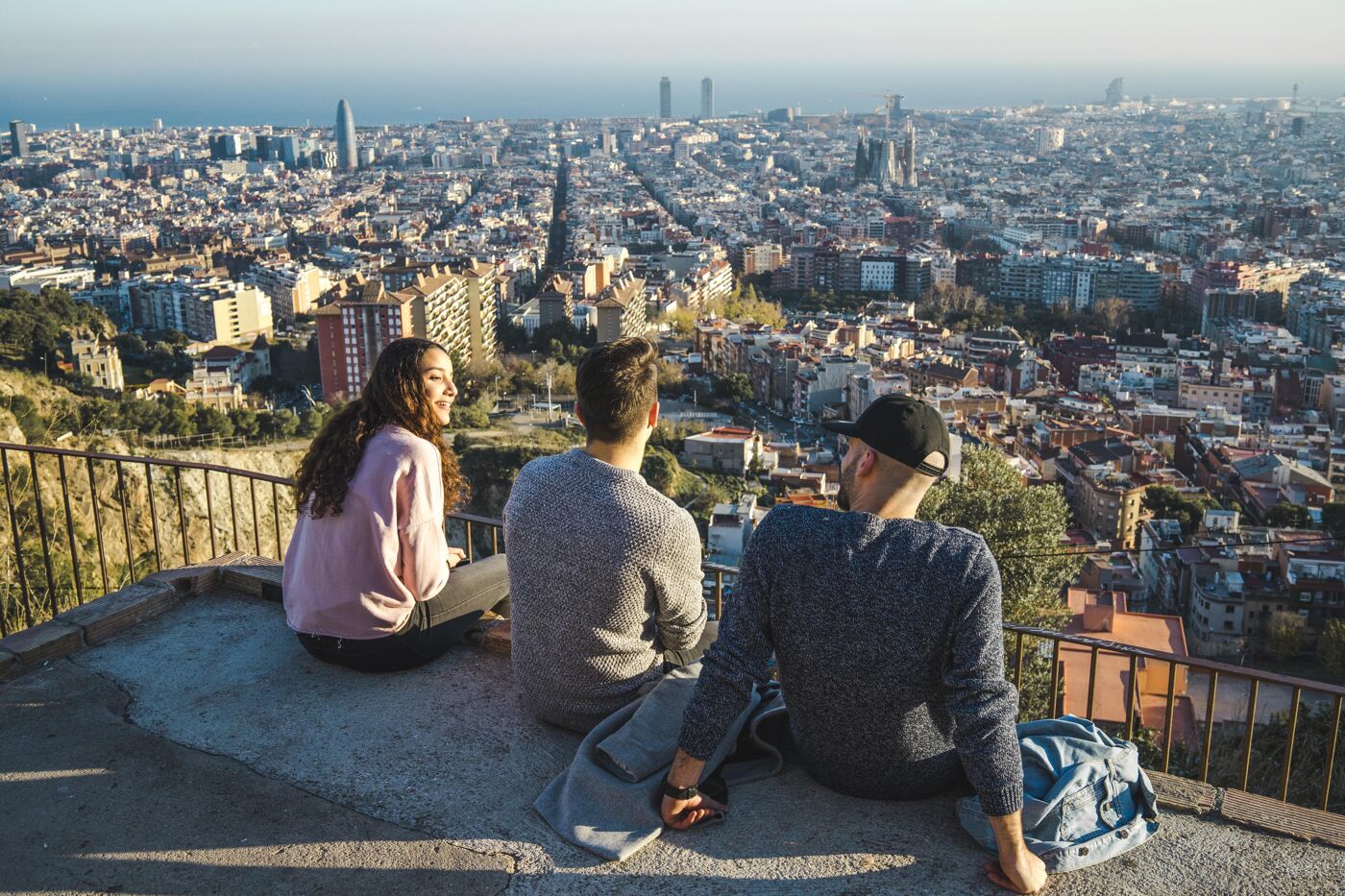 Spain, Barcelona, three friends sitting on a wall overlooking the city