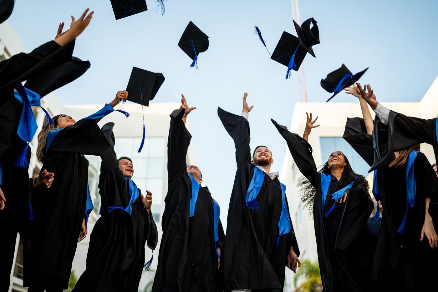 A group of graduates in caps and gowns joyfully toss their hats in the air.