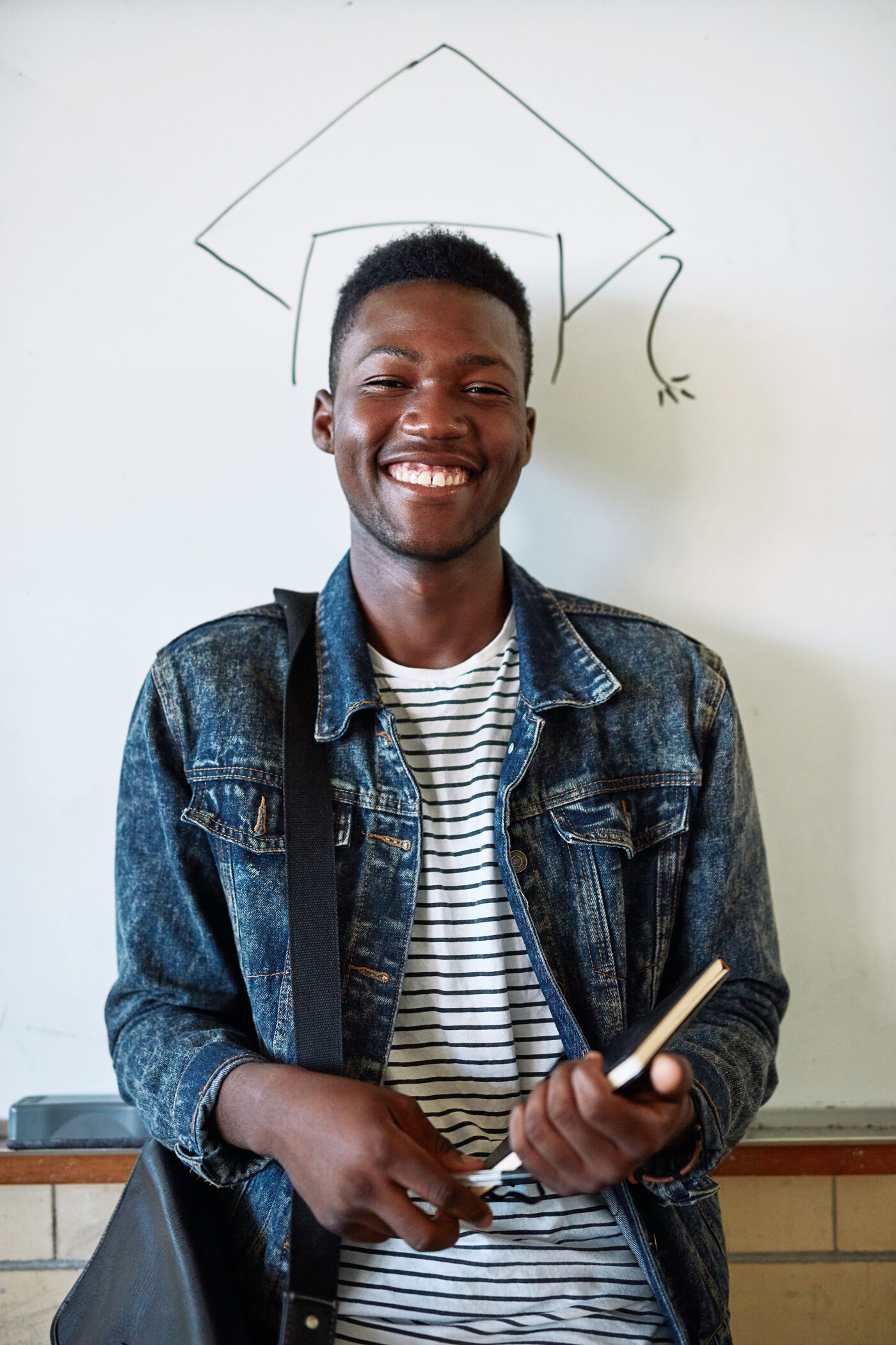 Portrait of a happy young man standing in front of a whiteboard with an illustrated graduation cap at university