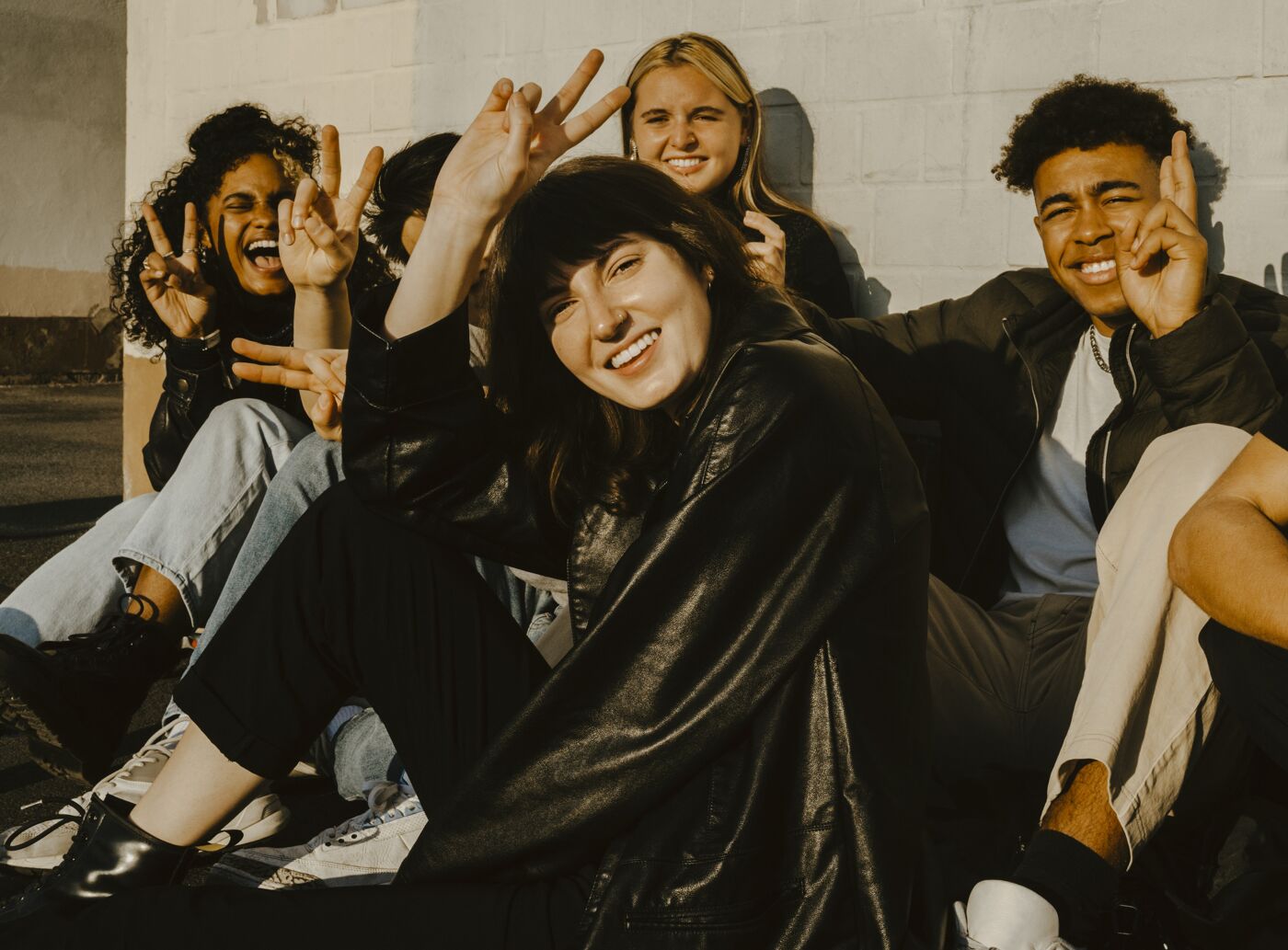 A group of jovial friends sitting outdoors, making playful gestures towards the camera.