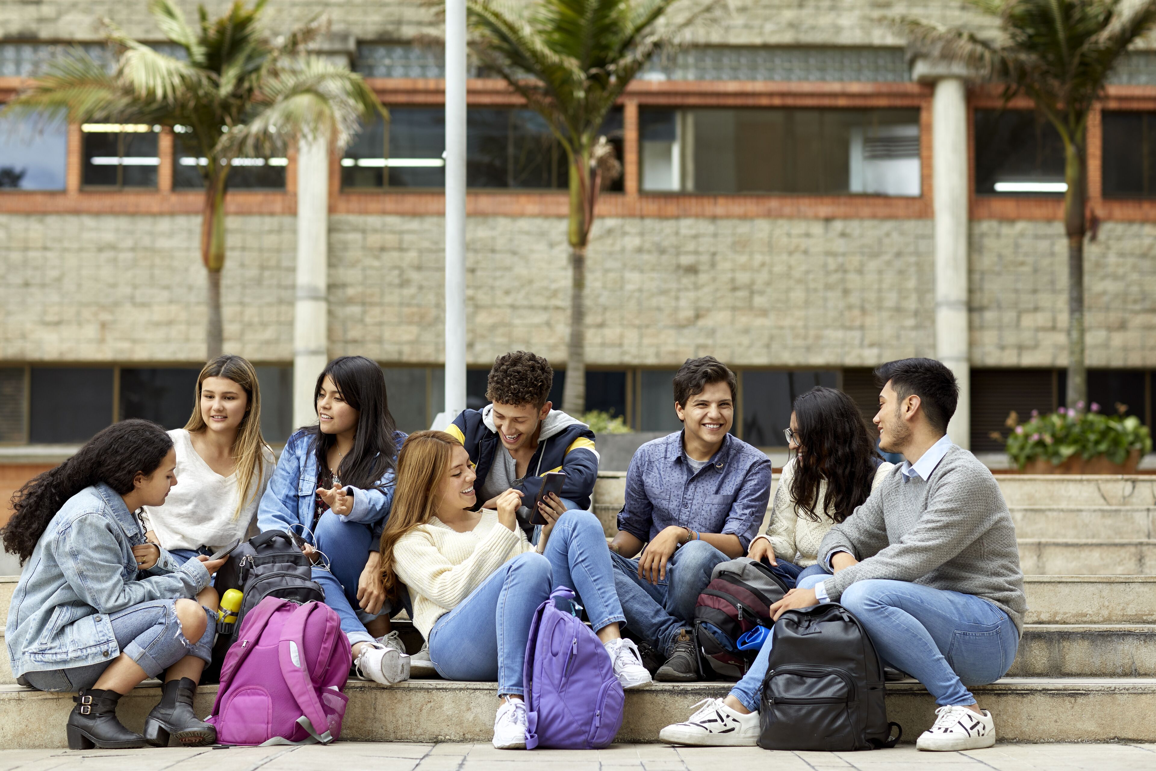 Smiling young students talking in campus. Happy male and female are sitting on staircase. They are wearing casuals.