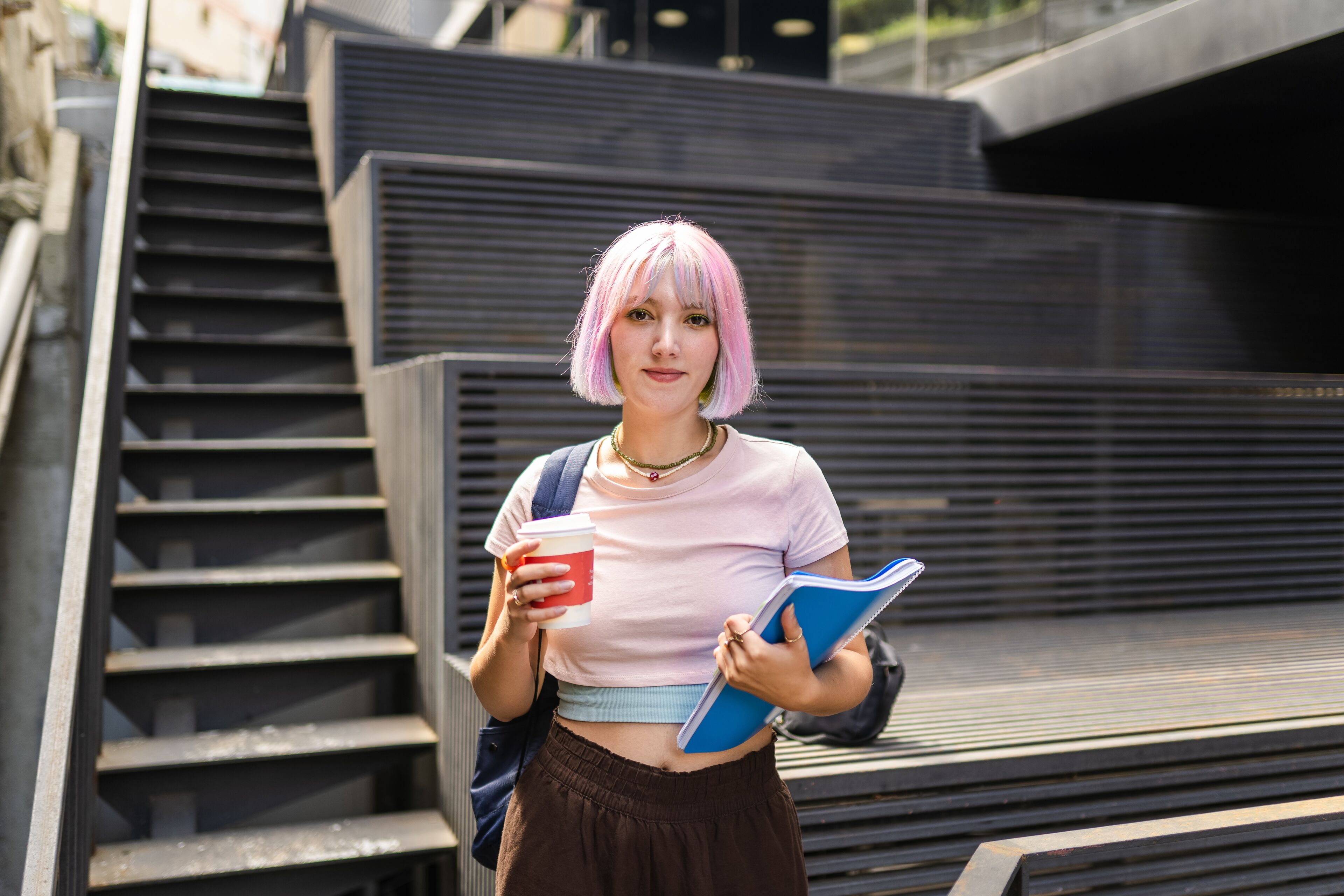 Image of young woman with colorful hair on university campus and holding sustainable coffee cup