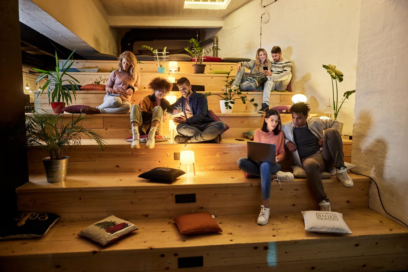 Large group of millennials using wireless technology on staircase at casual office.