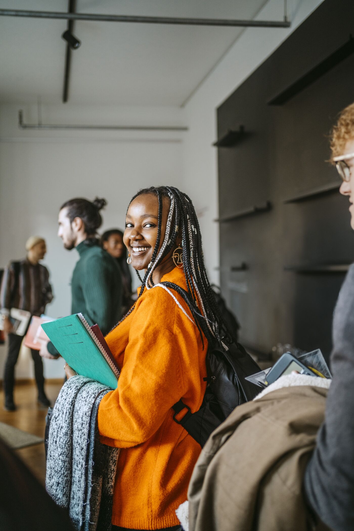 Portrait of smiling woman holding files and books by friend at community college