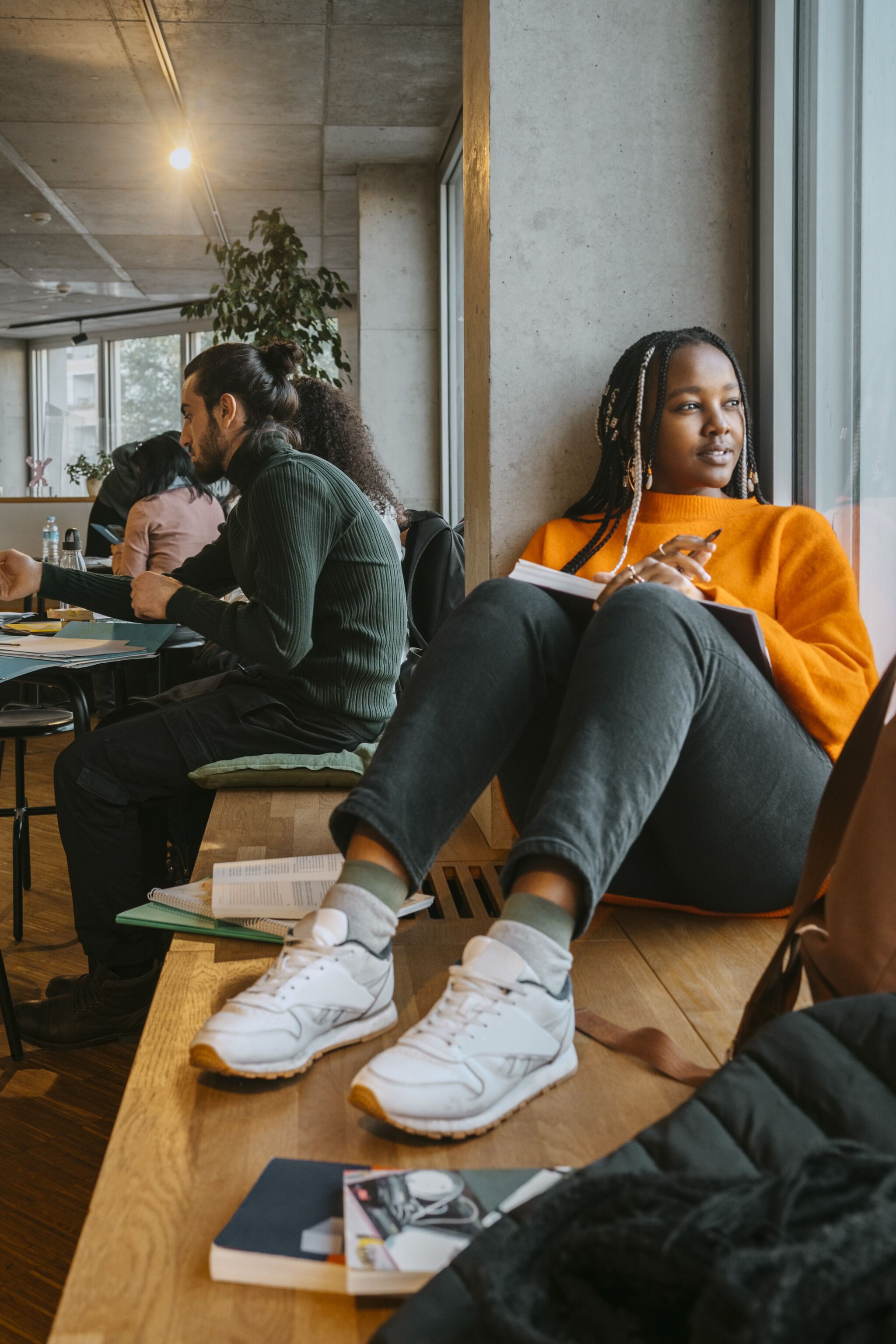 Full length of thoughtful young woman sitting with book in university cafeteria