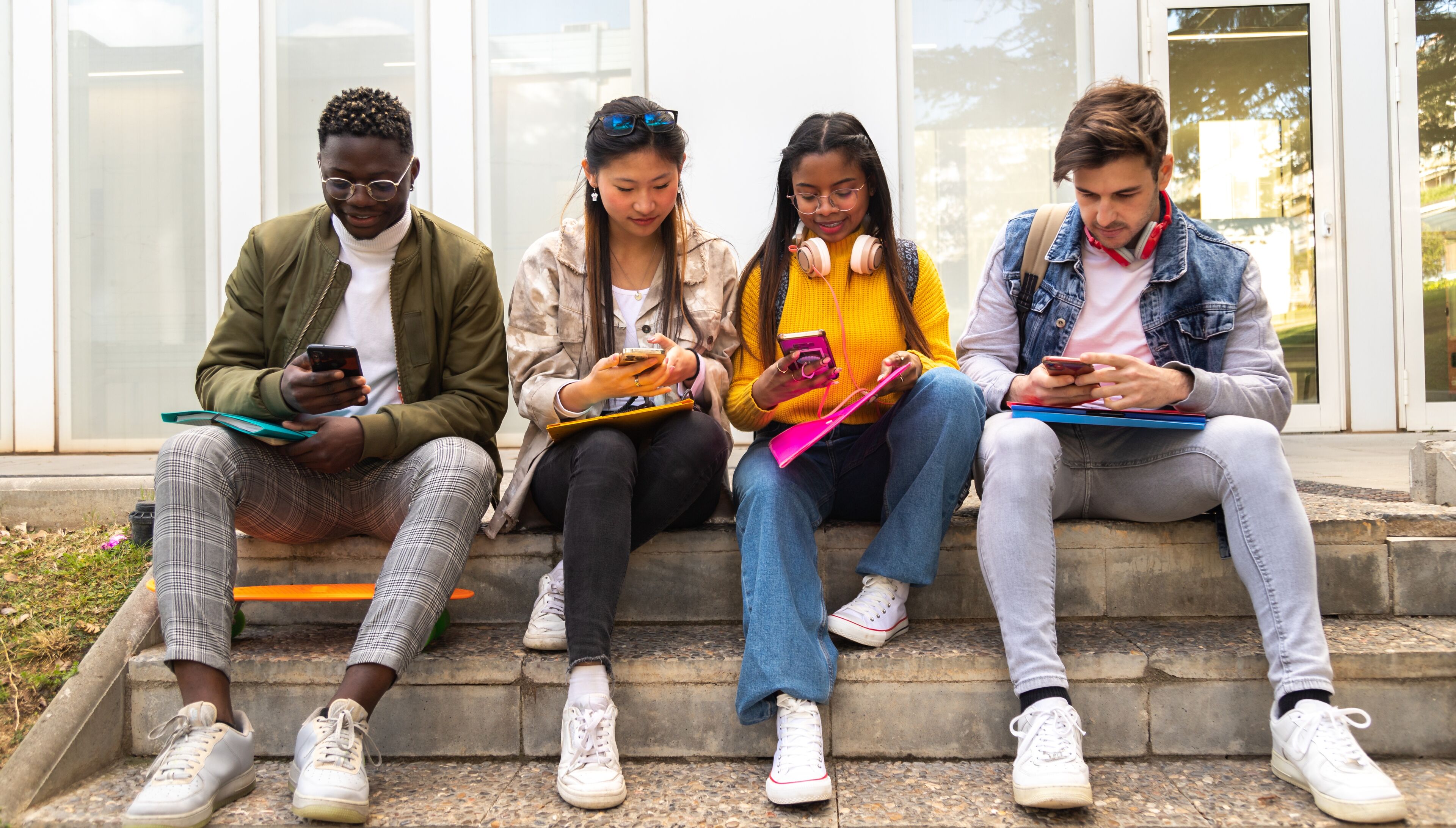 A diverse group of students sitting on steps, each absorbed in their own smartphone, depicting modern campus life.