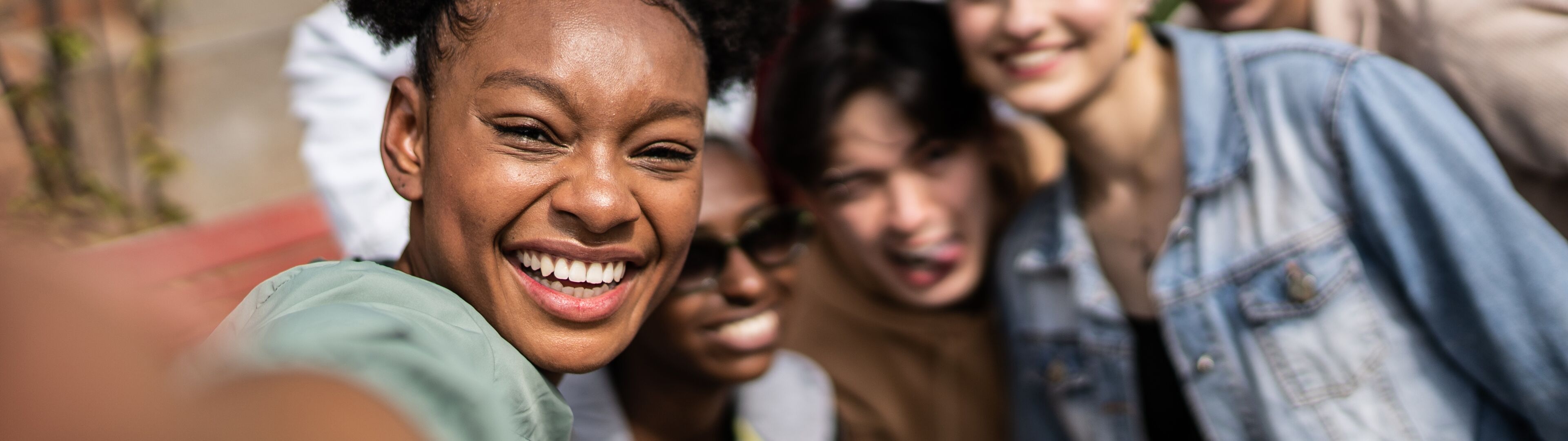 Un selfie grupal vibrante con una joven en primer plano y amigos de varias etnias sonriendo detrás.