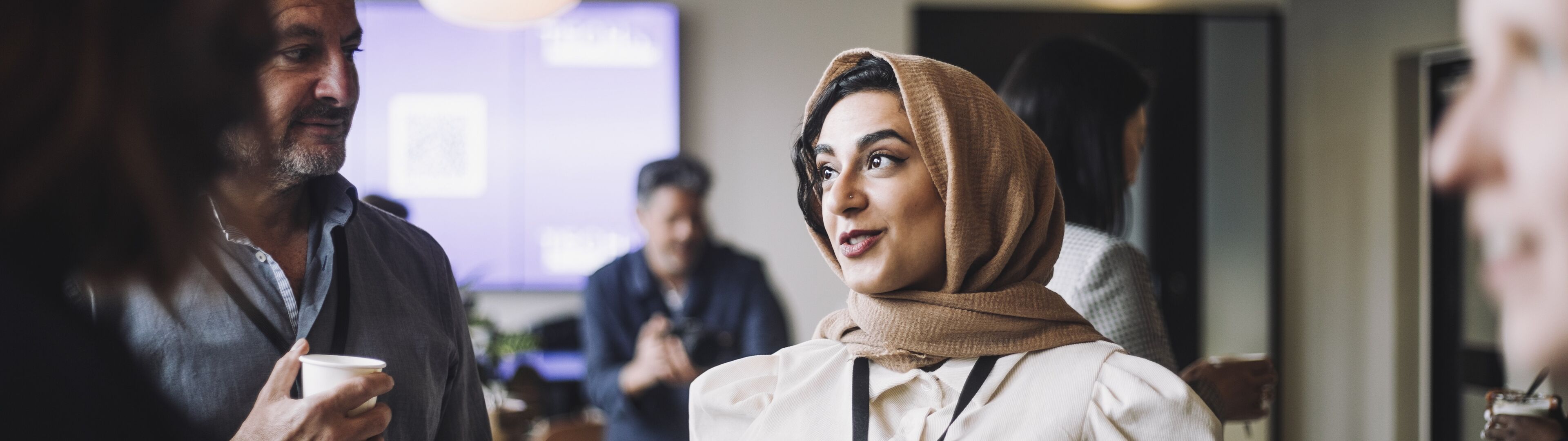 Une femme portant un hijab converse avec des collègues autour d'un café dans une ambiance détendue et contemporaine de réseautage.