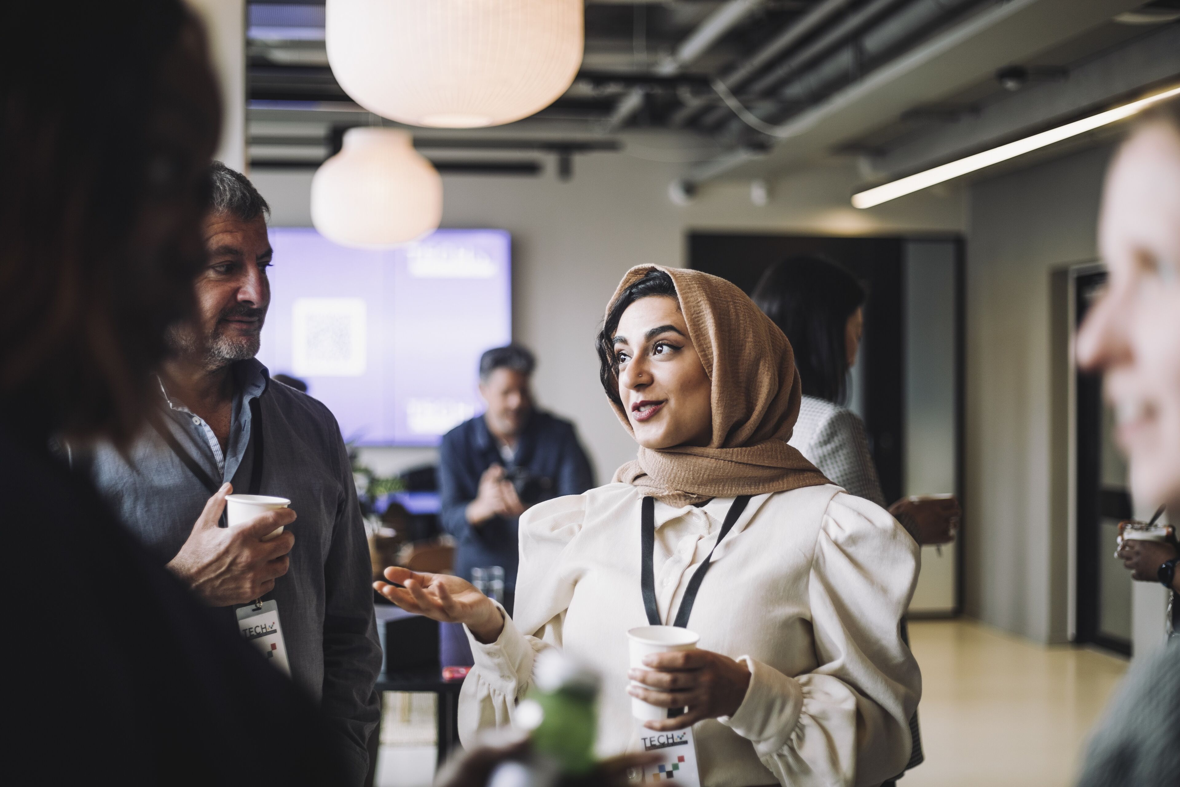 A woman in a hijab converses with colleagues over coffee in a relaxed, contemporary networking event setting.
