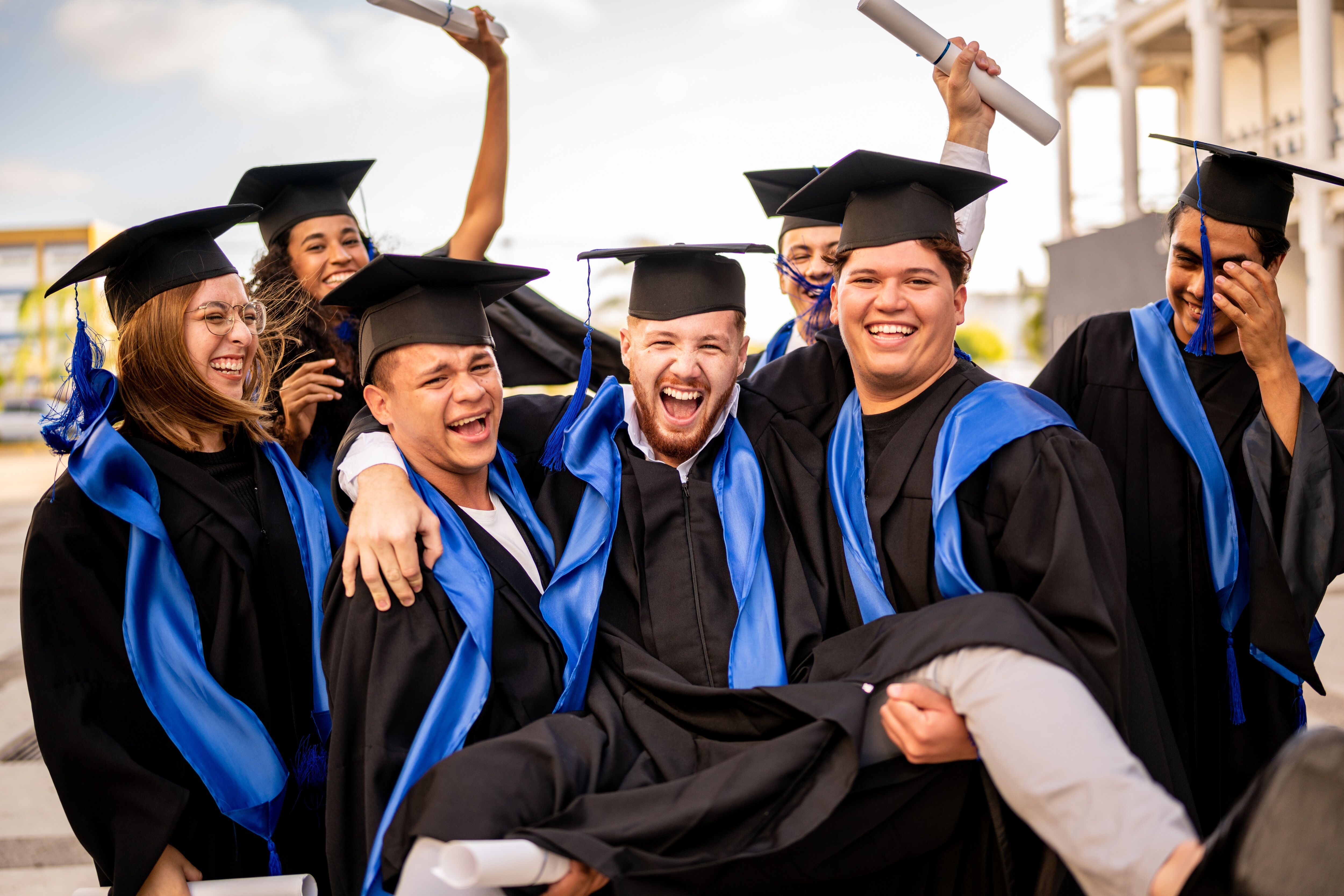 Portrait of young graduate man being carried by his graduate friends at graduation