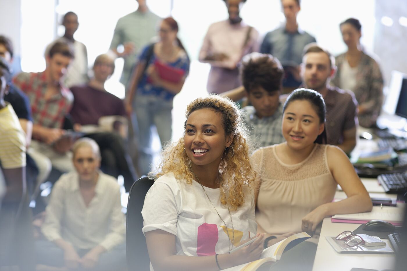 Diverse group of students attentively listening in a brightly lit classroom setting.