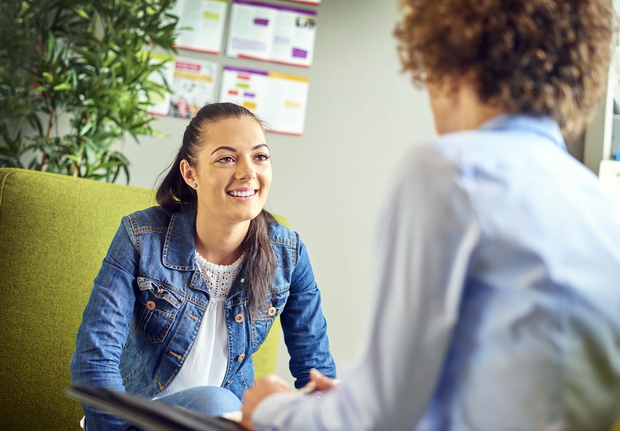 A smiling woman in casual attire engaged in a conversation with another person.