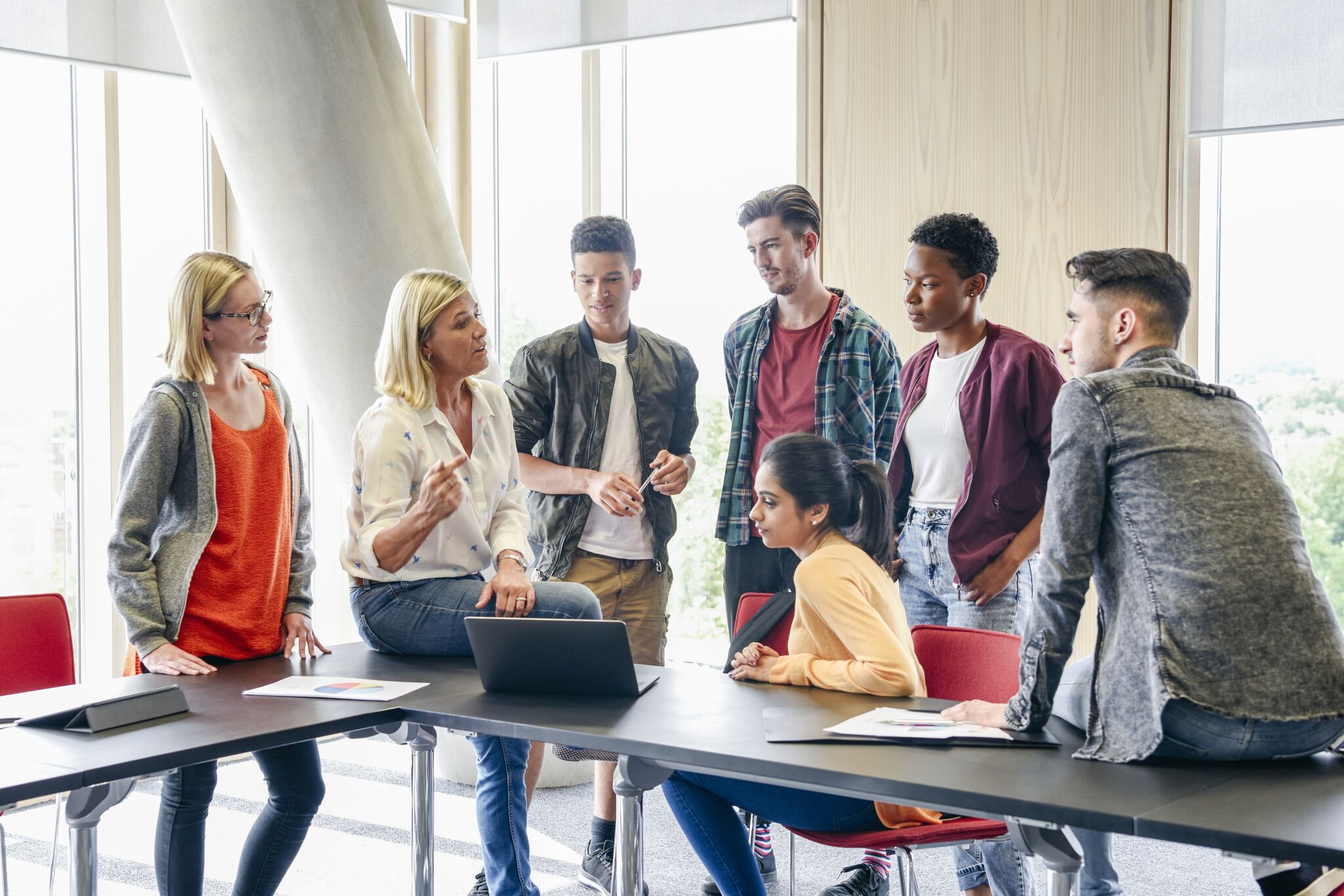 A diverse group of professionals engaged in a discussion around a table with laptops.