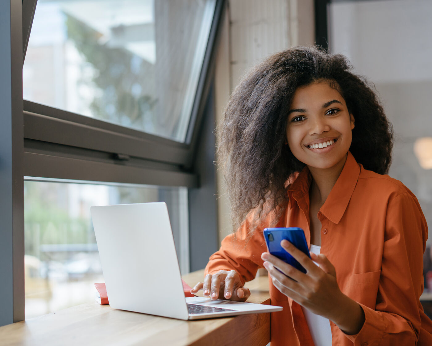 Young beautiful woman working in office. Portrait of smiling African American businesswoman using laptop computer and internet, holding mobile phone. Successful business concept