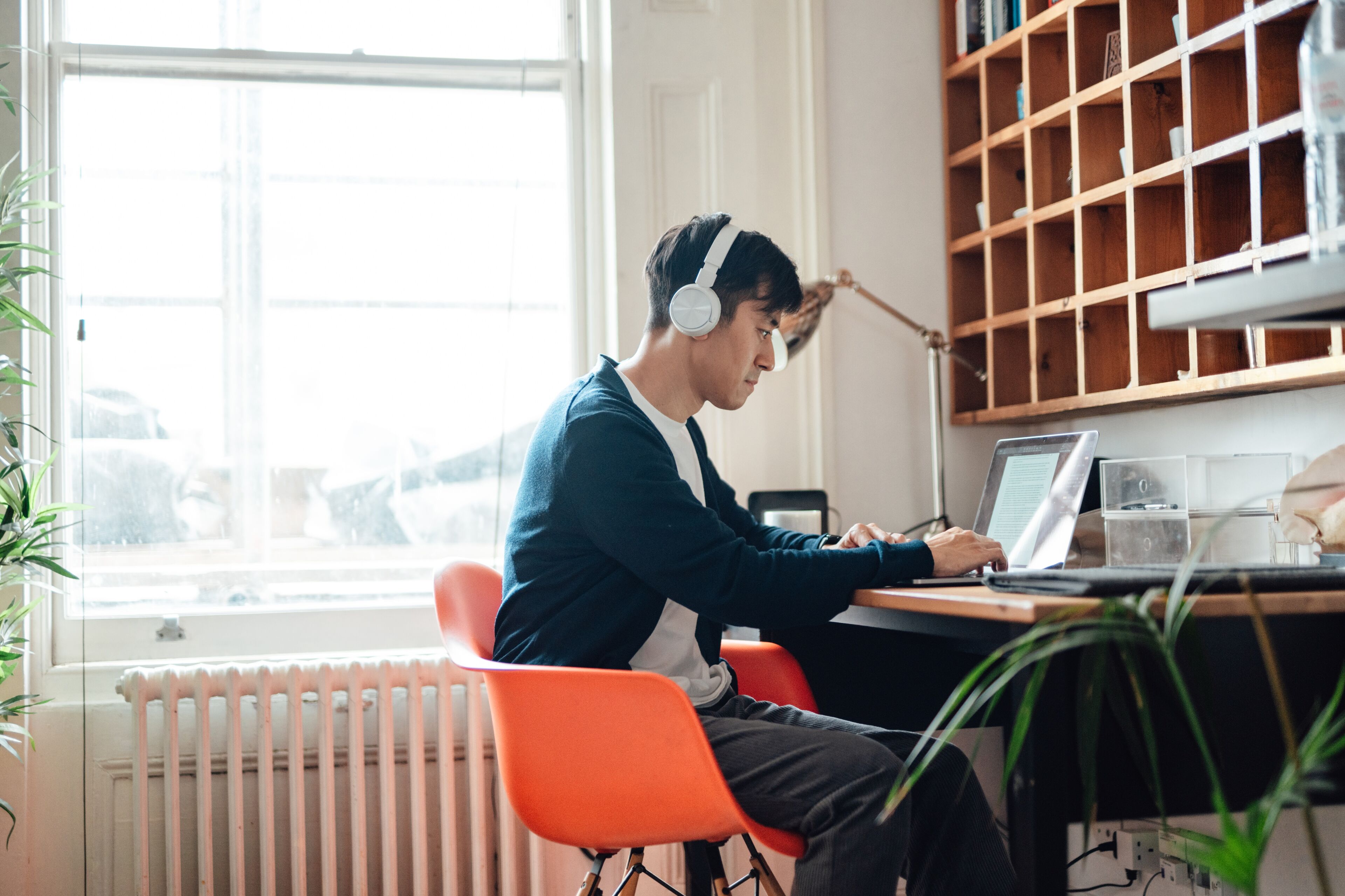 Young Asian man with headphones, taking online course with laptop at home. Adult learning. Online university classes. Working from home.