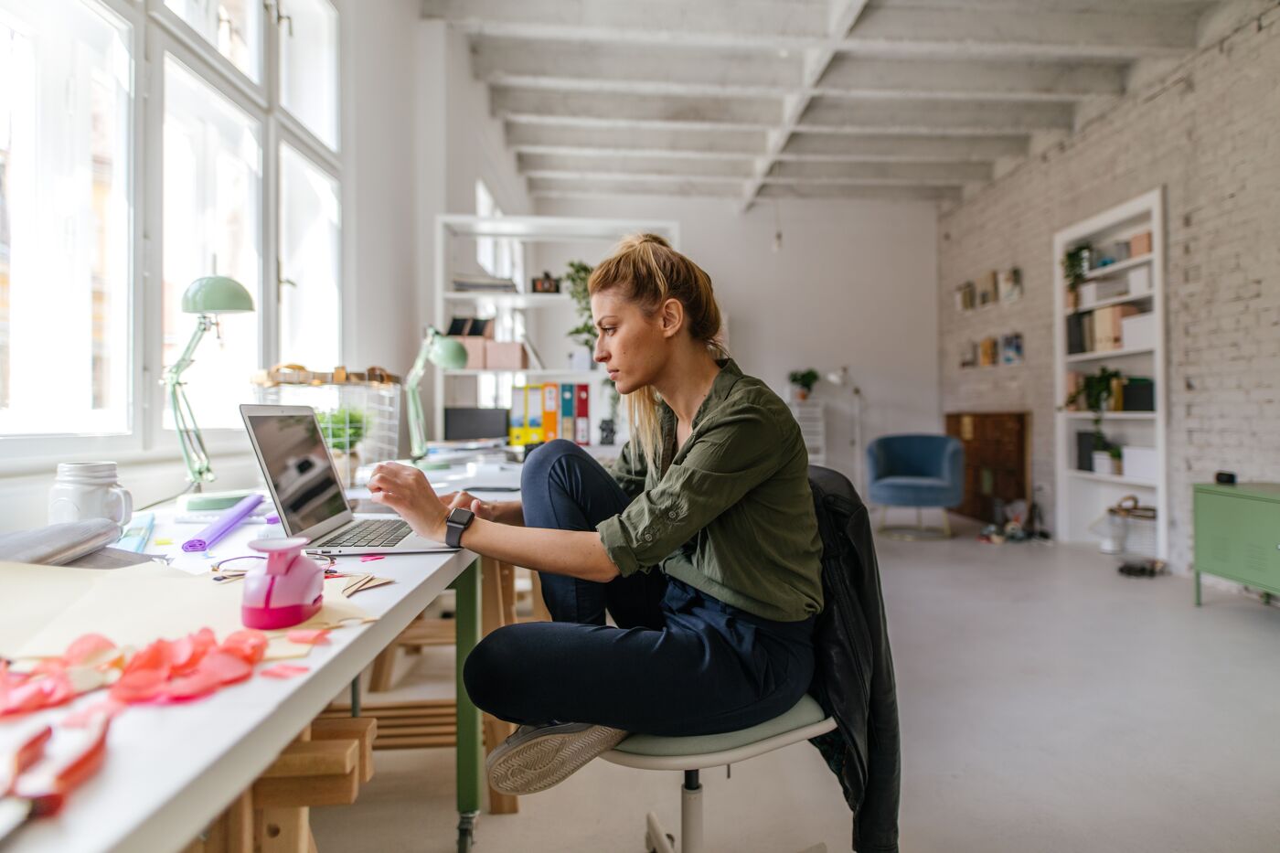 Photo of a woman sitting cross-legged in her chair, working online from a home office