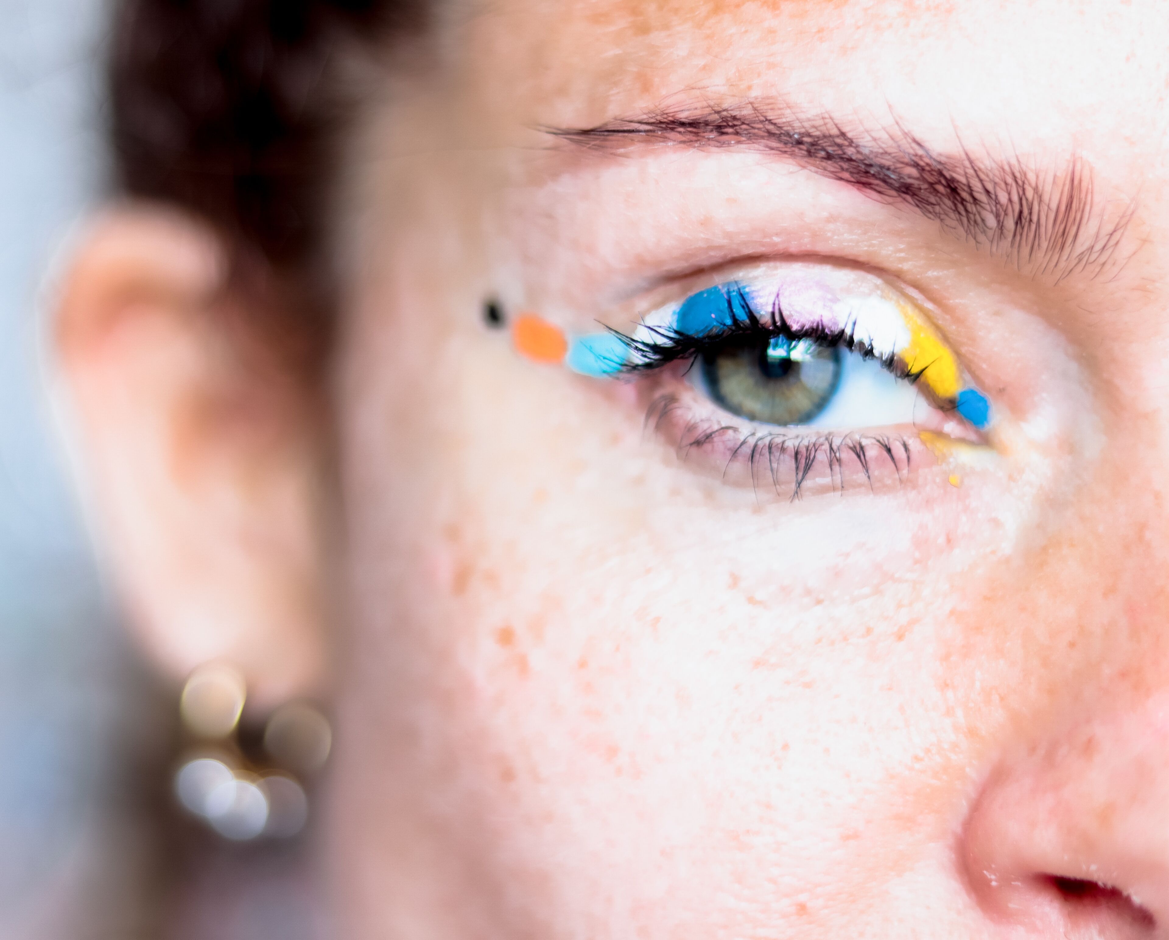 Primer plano del ojo de una persona con delineador artístico en tonos vibrantes de azul, amarillo y naranja.