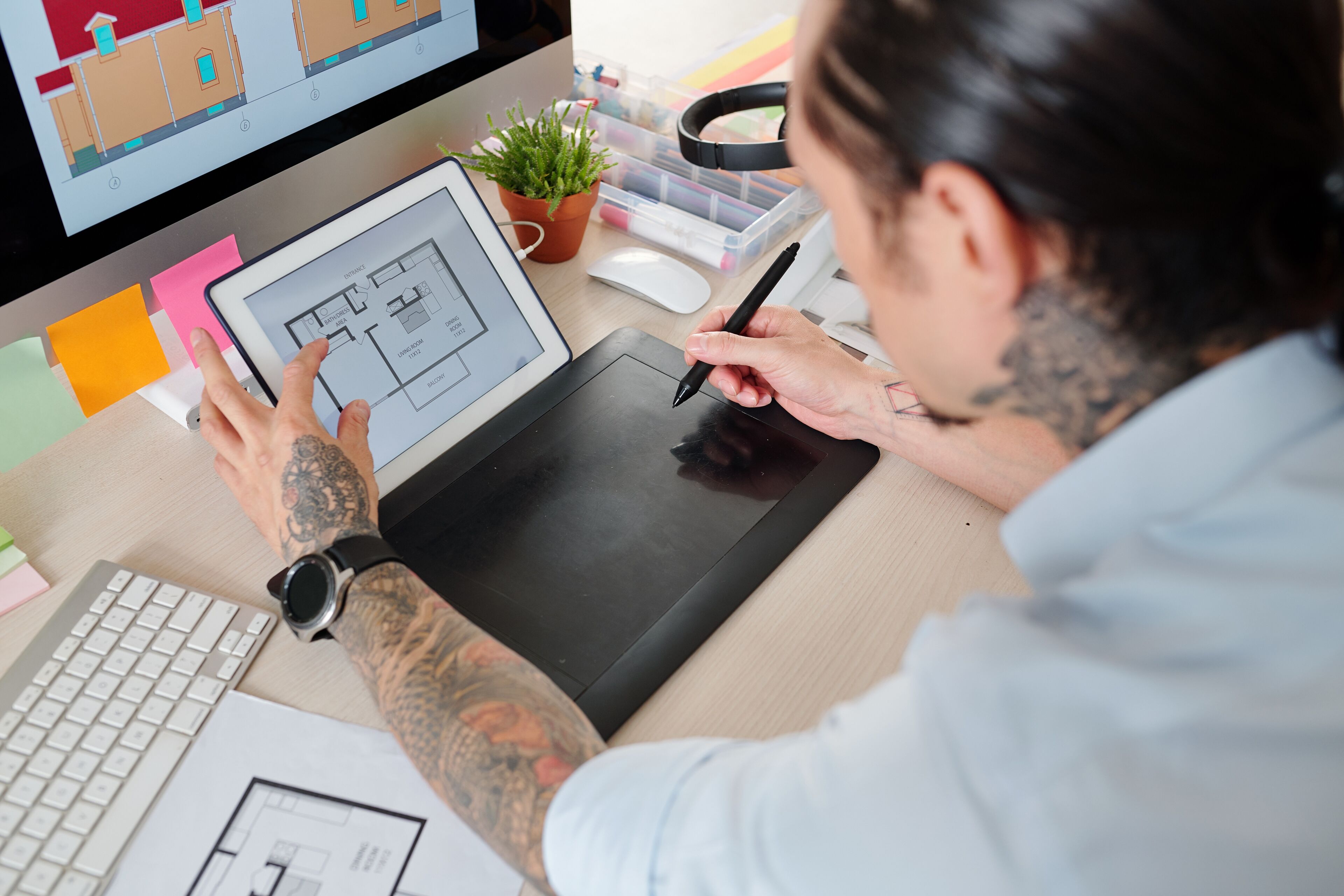 An architect drafts a detailed floor plan on a digital tablet with a stylus, with a secondary monitor showing additional design work.