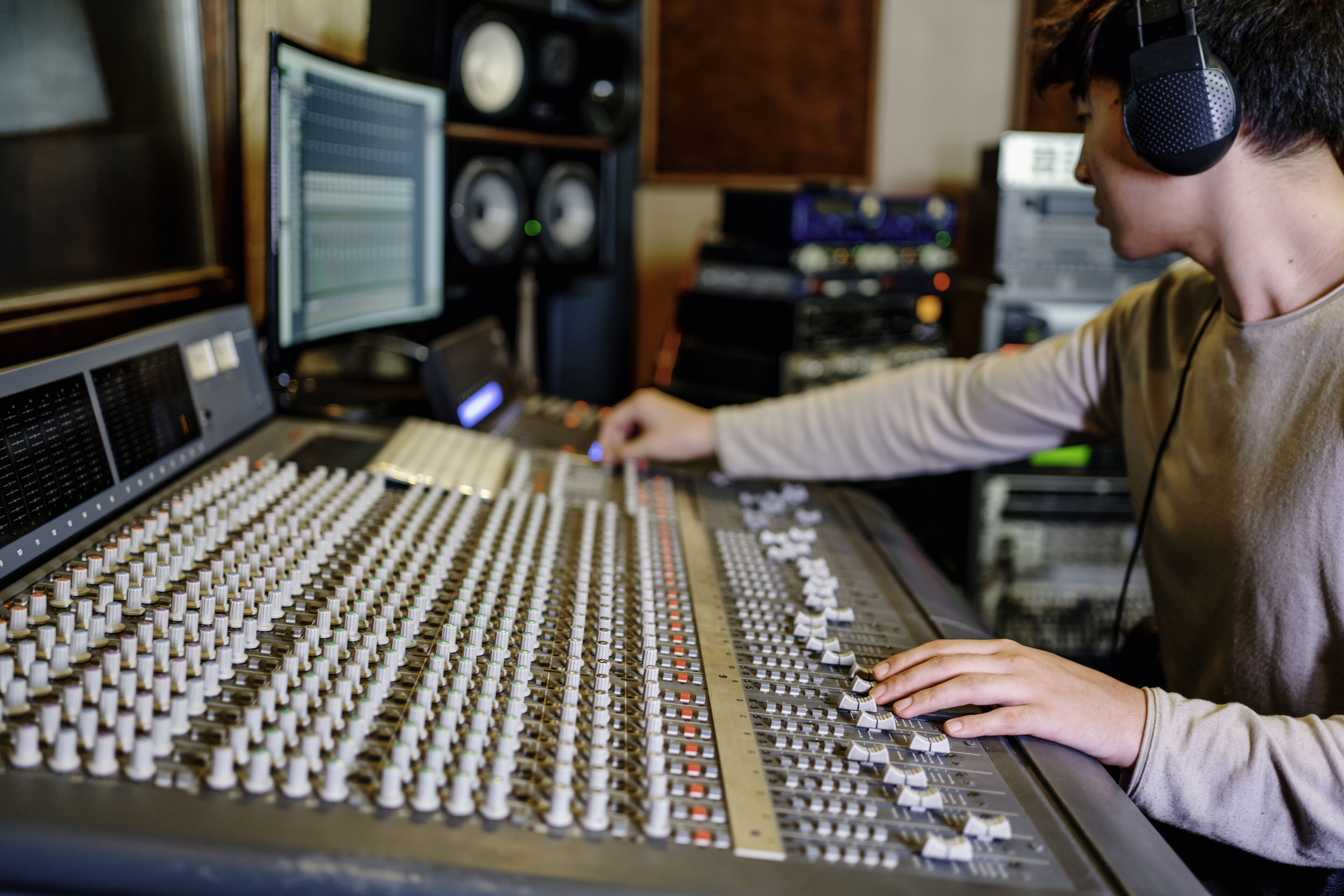 Person adjusting audio levels on a professional mixing console in a studio setting.