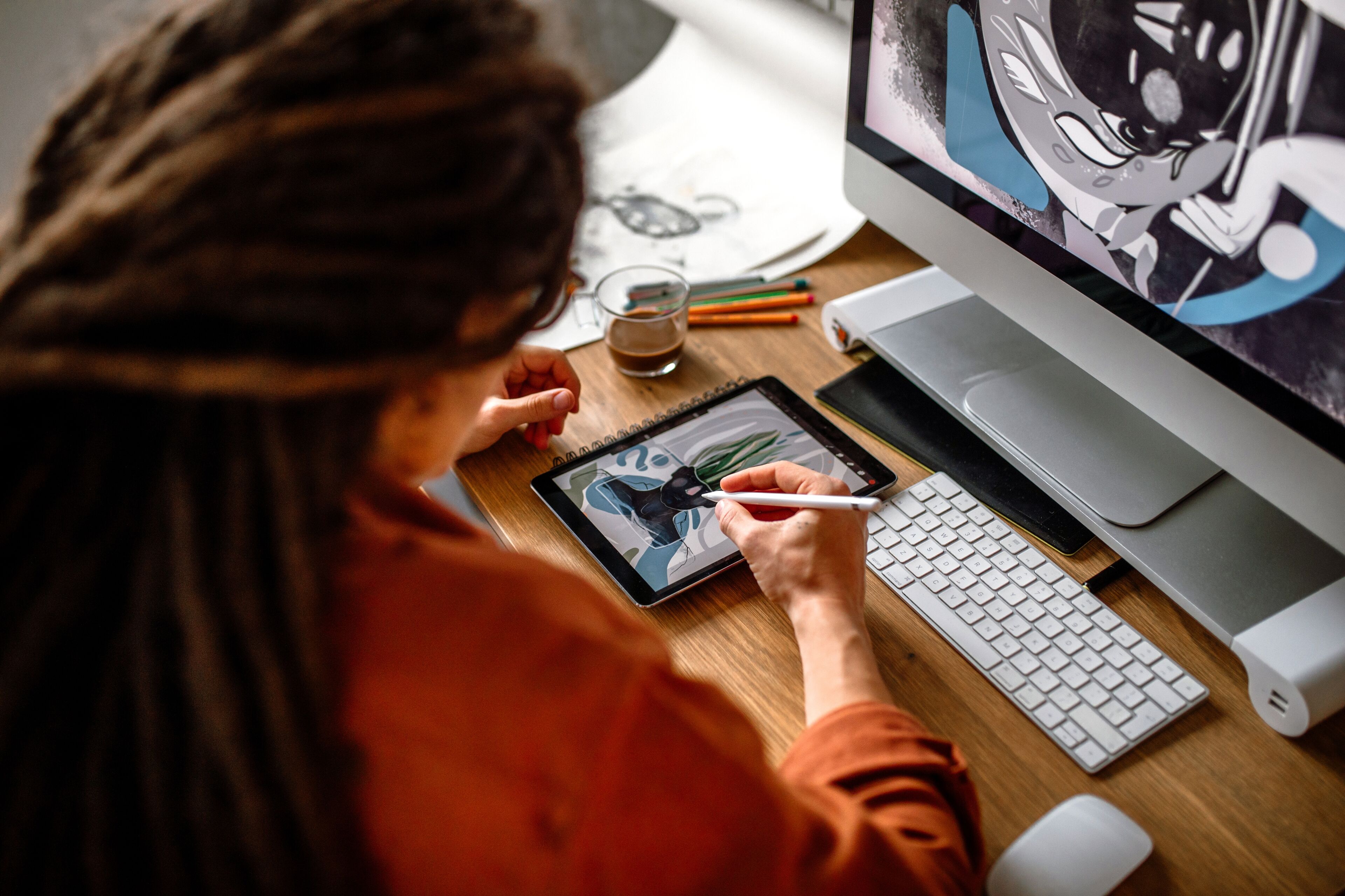 Un(a) artista esboza en una tableta digital con un lápiz, refiriéndose a una ilustración de personaje en un monitor.