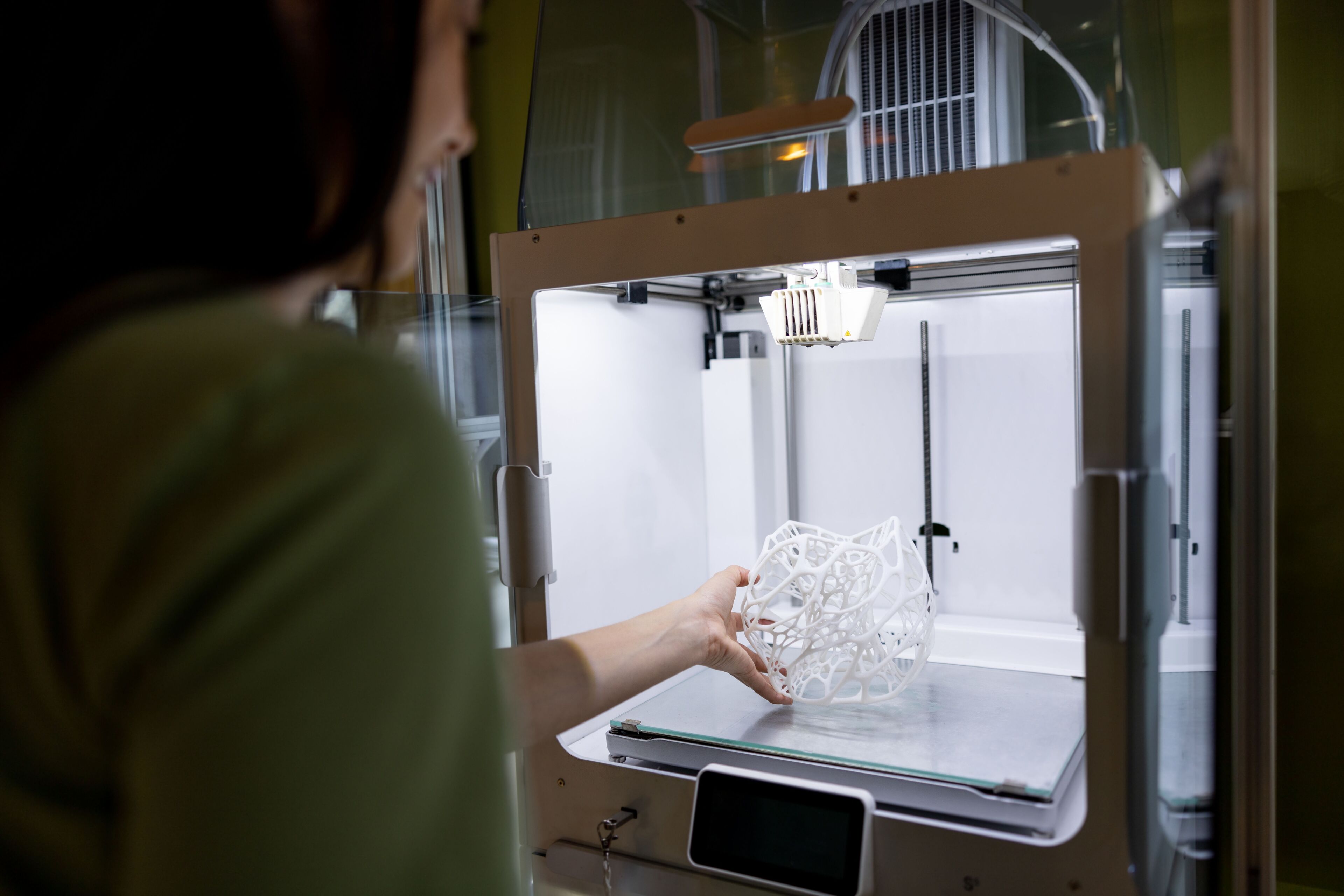 Una persona recull un objecte 3D acabat d'imprimir de la plataforma de construcció d'una impressora 3D professional.