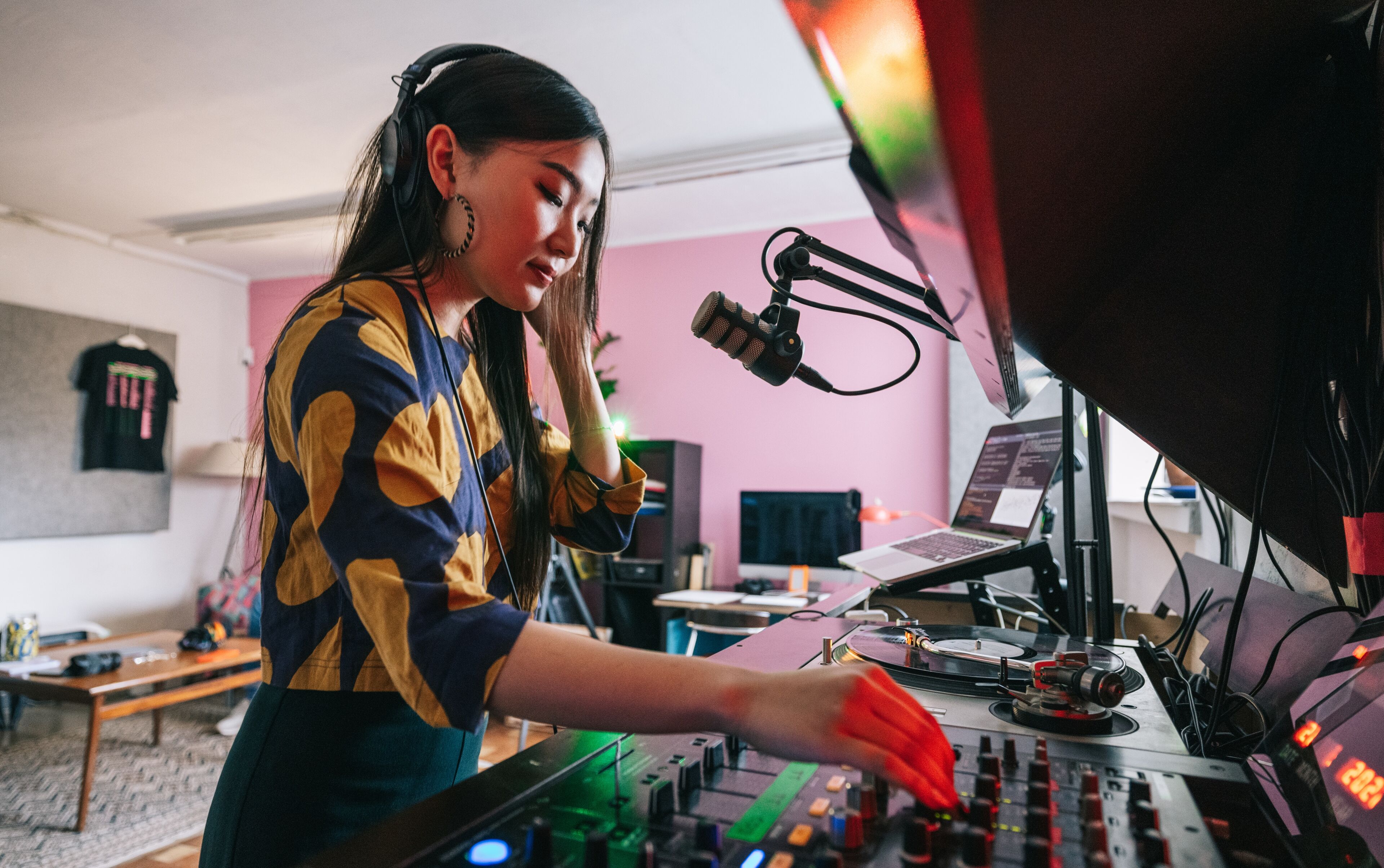 Une DJ concentrée avec des écouteurs mixe des pistes sur une table de mixage professionnelle dans son studio maison coloré.