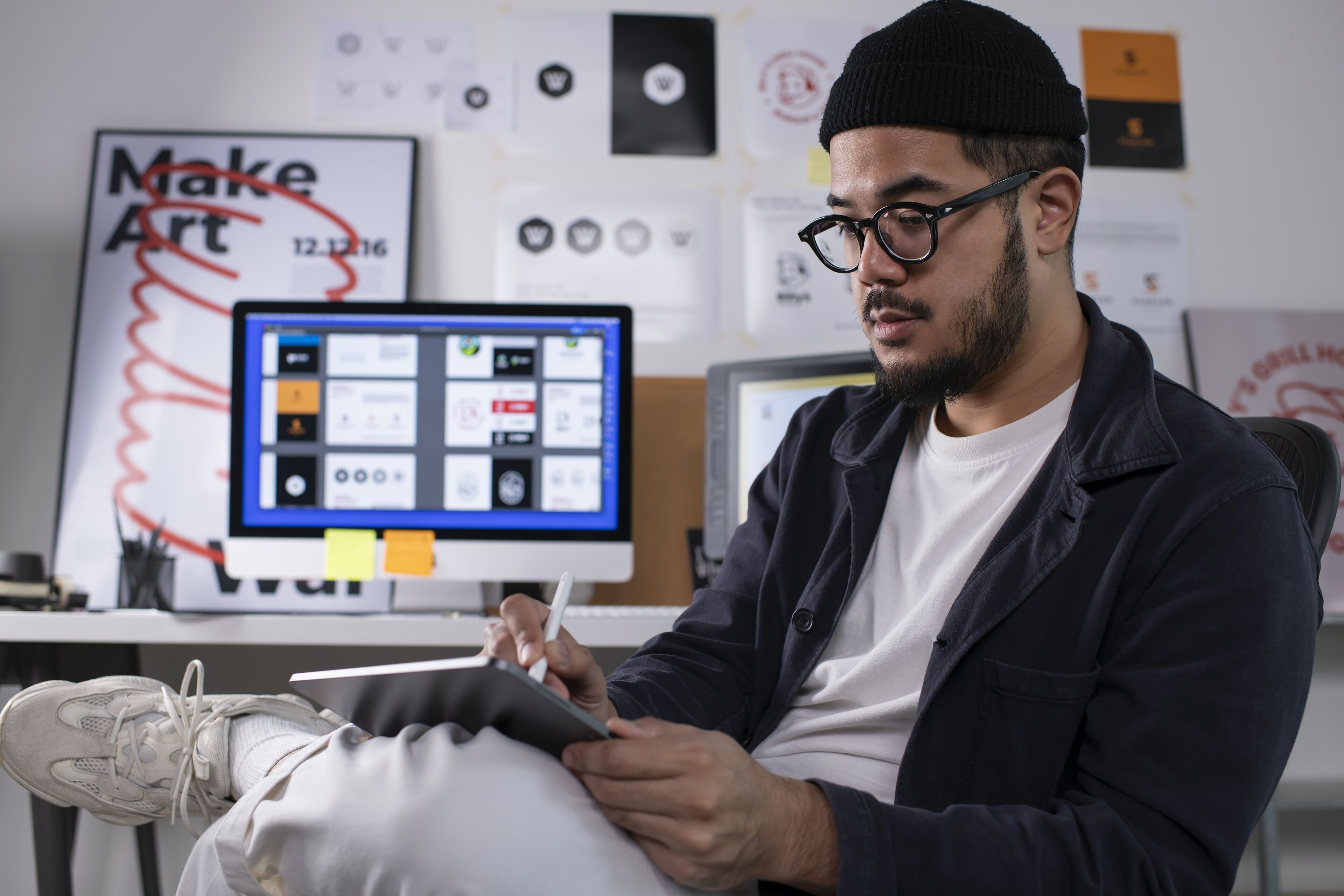 Un artiste numérique masculin concentré dessine sur une tablette dans un studio créatif, entouré d'inspirations de design.