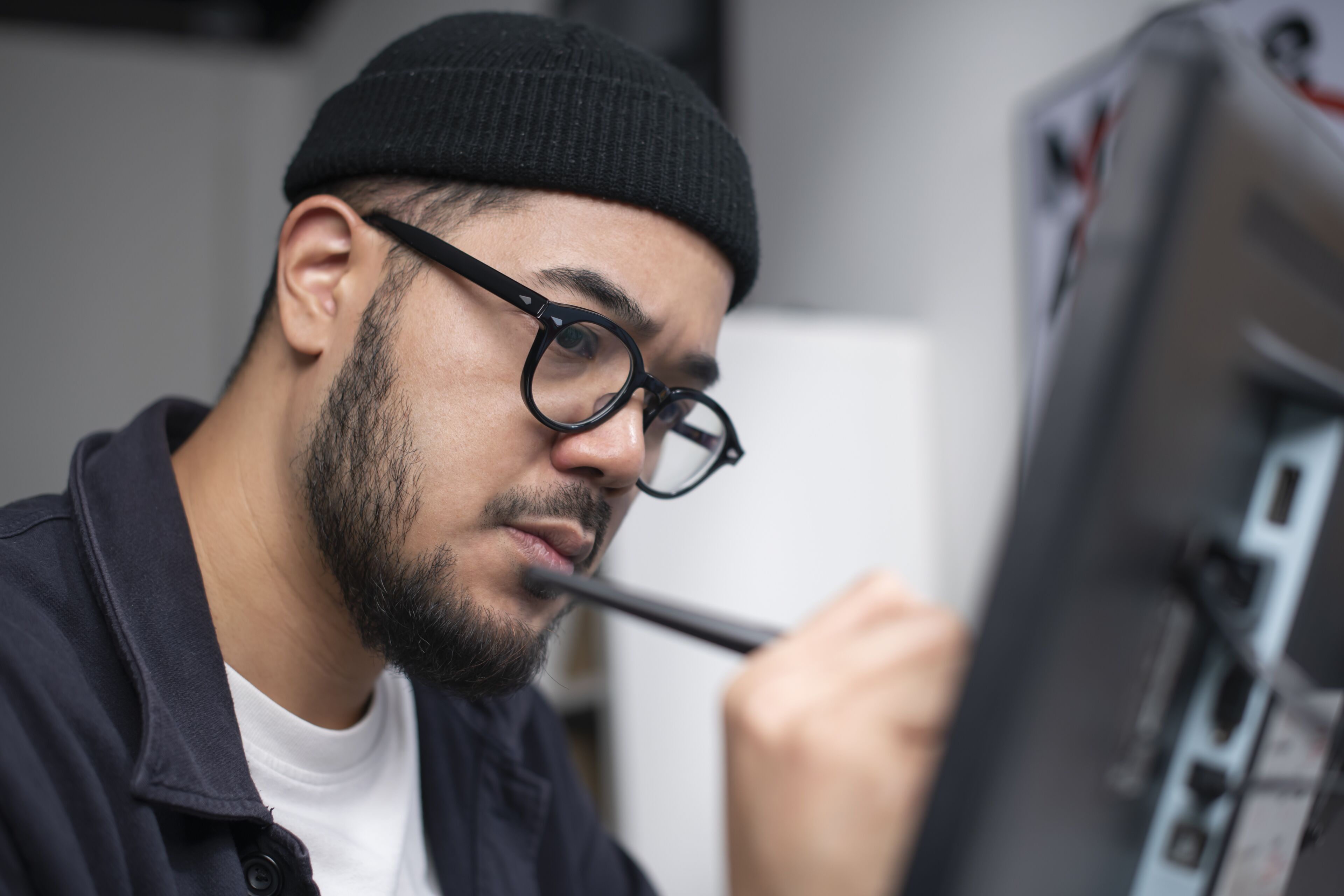 Un graphiste masculin concentré avec des lunettes et un bonnet édite sur une tablette graphique avec un stylet.