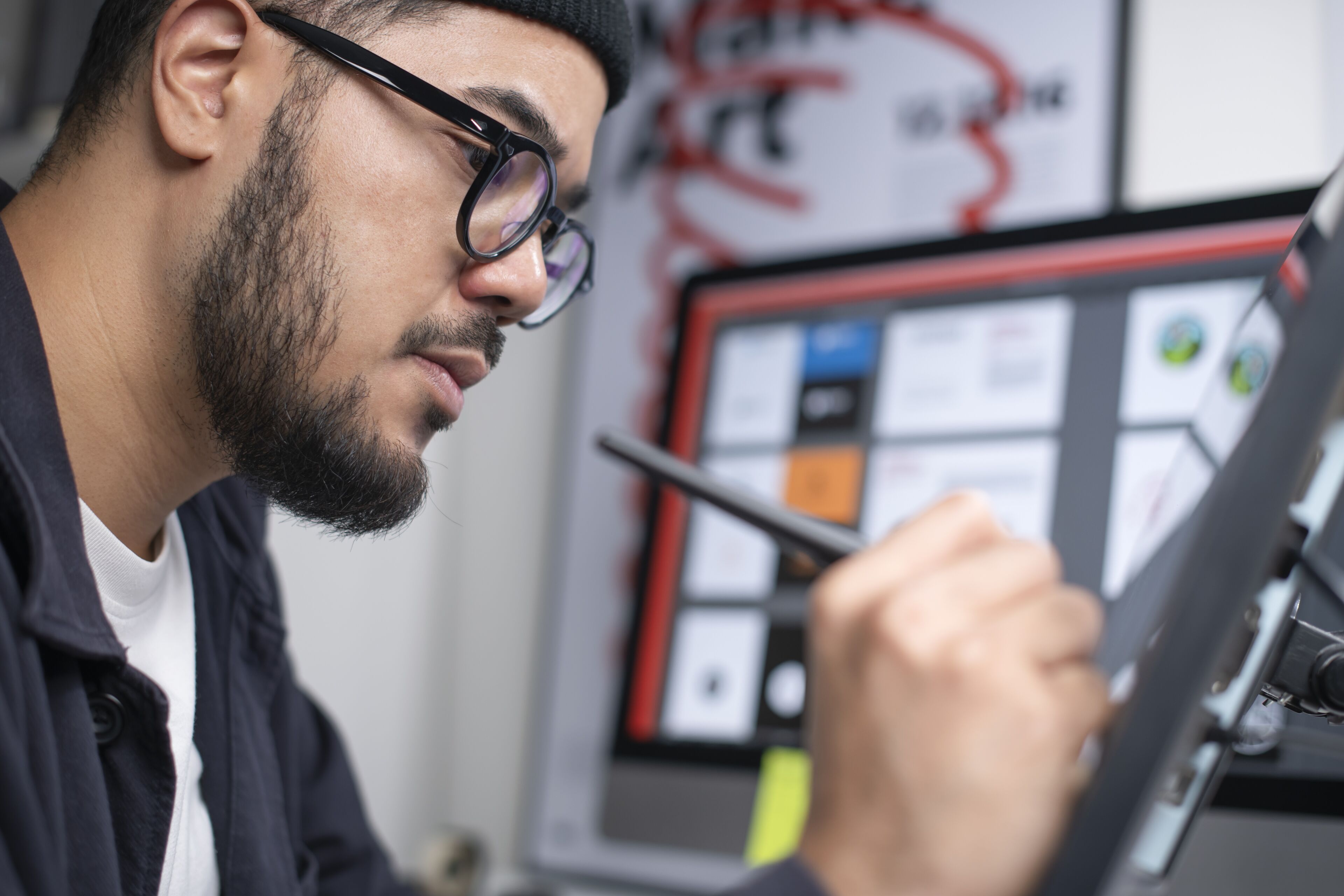 Un graphiste homme concentré avec des lunettes utilisant un stylet sur une tablette graphique numérique dans un espace de création.