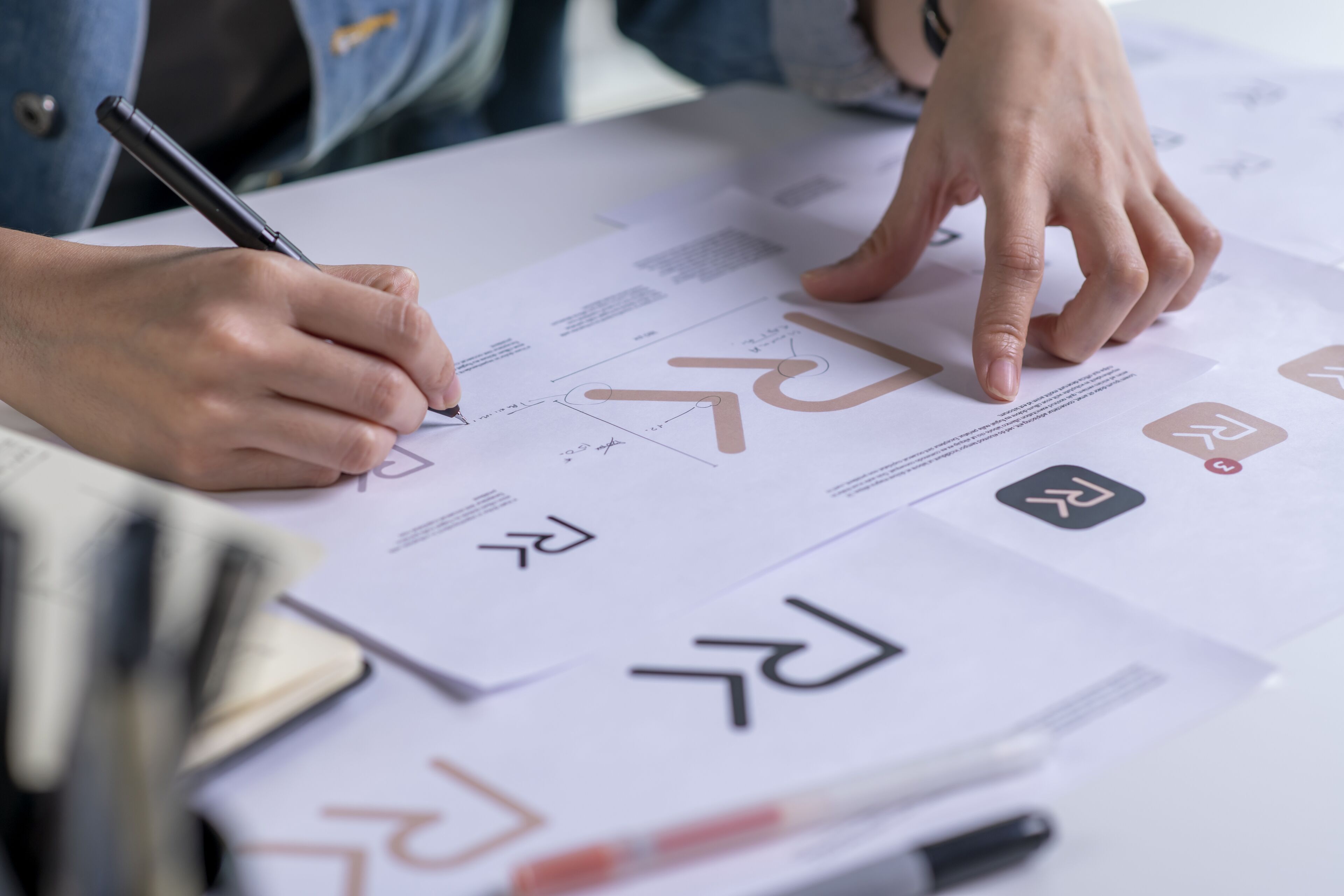Une personne examine et annote un ensemble de symboles de design graphique, possiblement pour une marque, stylo en main.