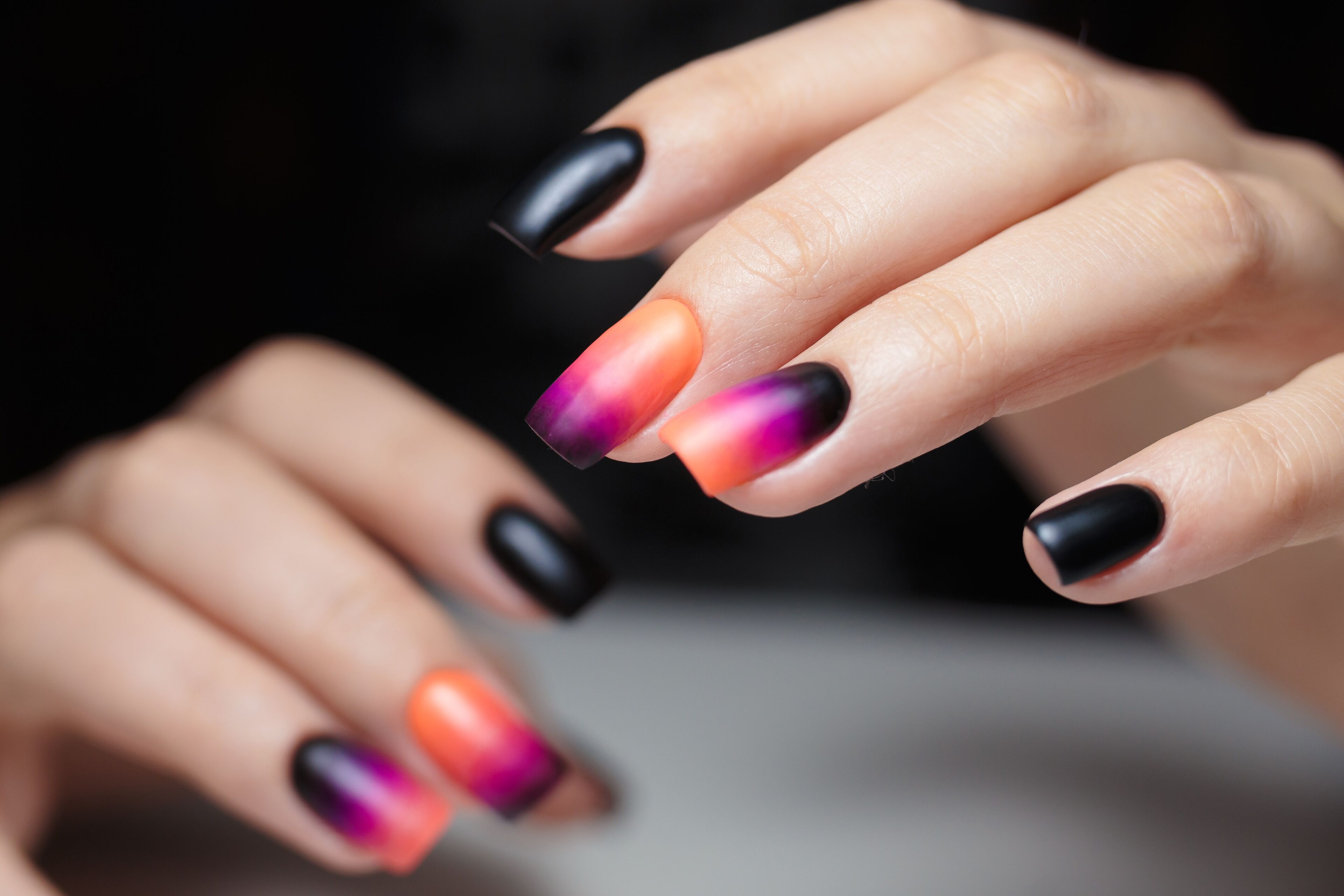 Close-up of a hand with nails painted in a black-to-vibrant gradient design.