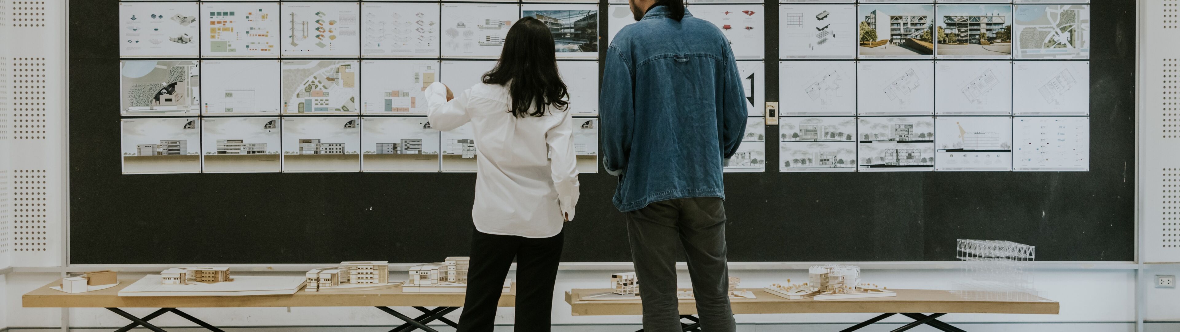 Two professionals evaluating architectural designs displayed on a board in a modern studio setting.