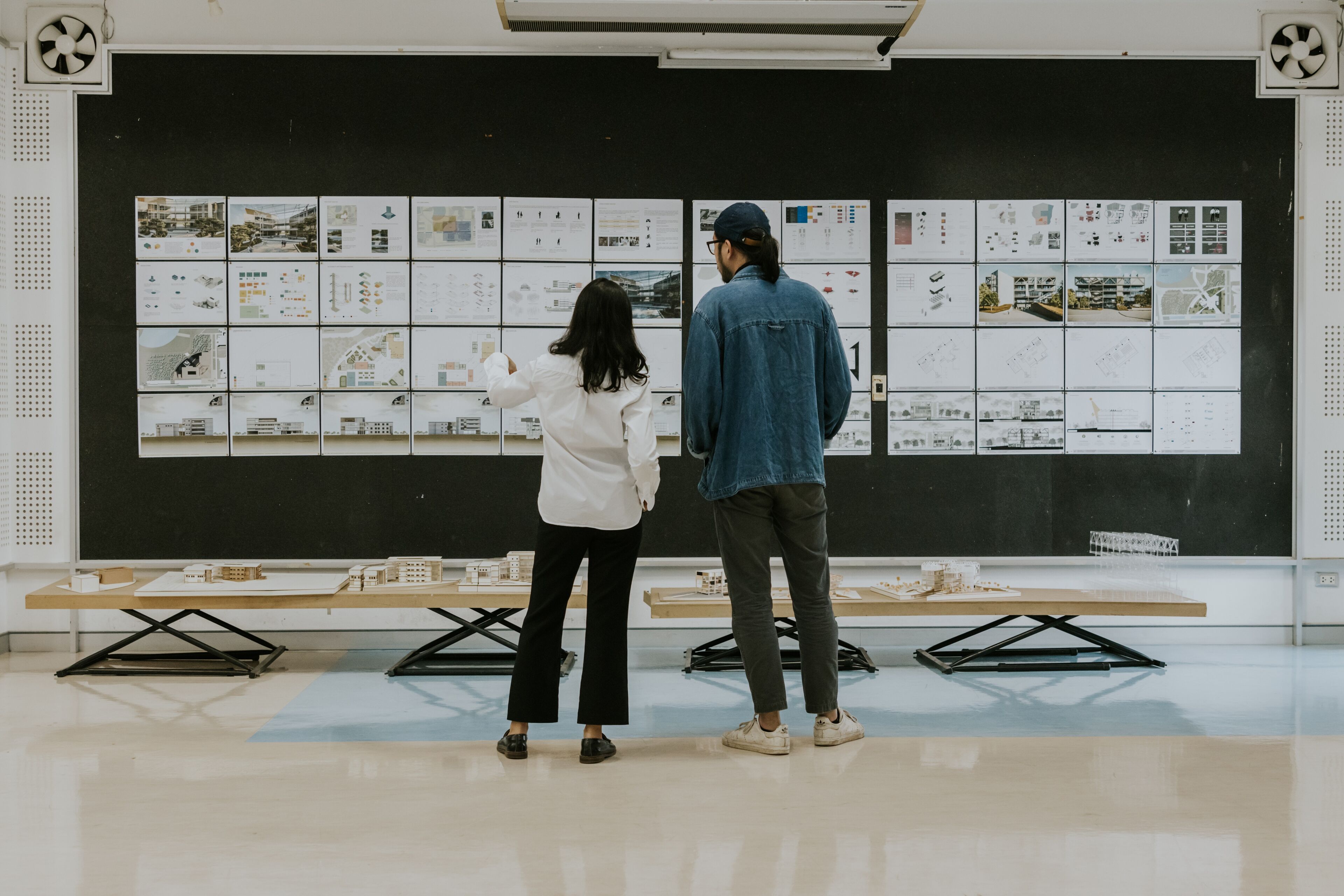 Two professionals evaluating architectural designs displayed on a board in a modern studio setting.