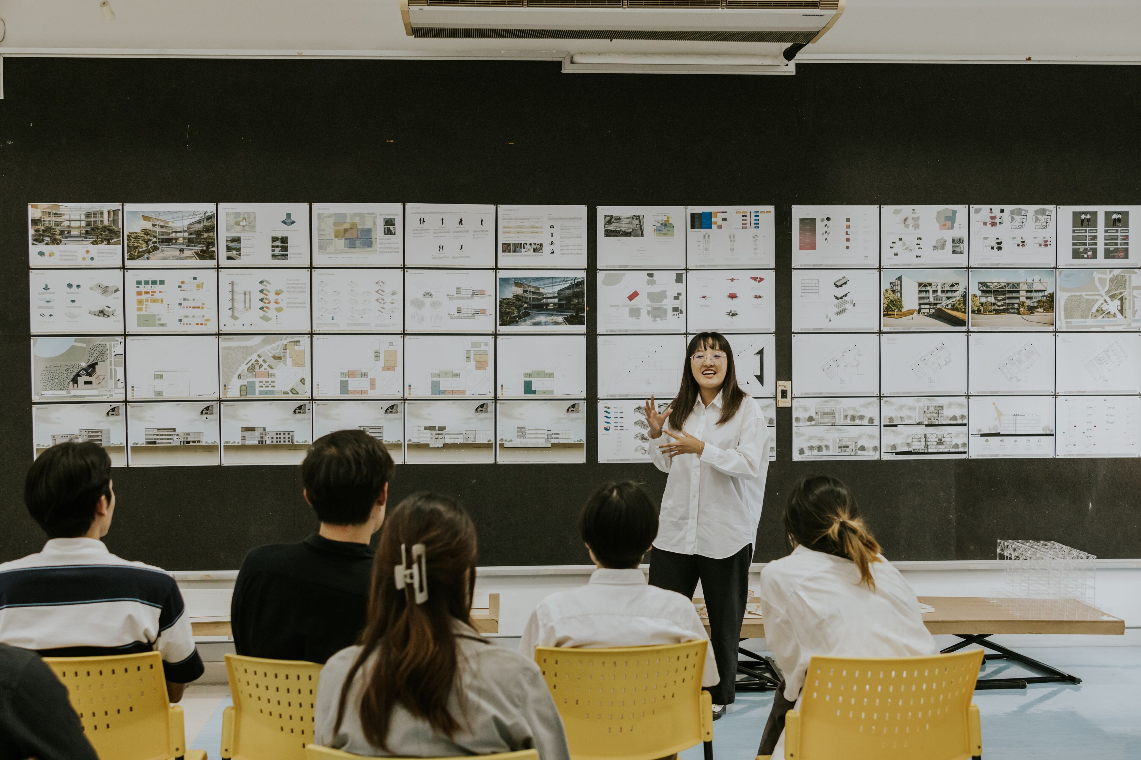 Una arquitecta femenina presenta planes de diseño a un grupo de oyentes atentos en un aula moderna.