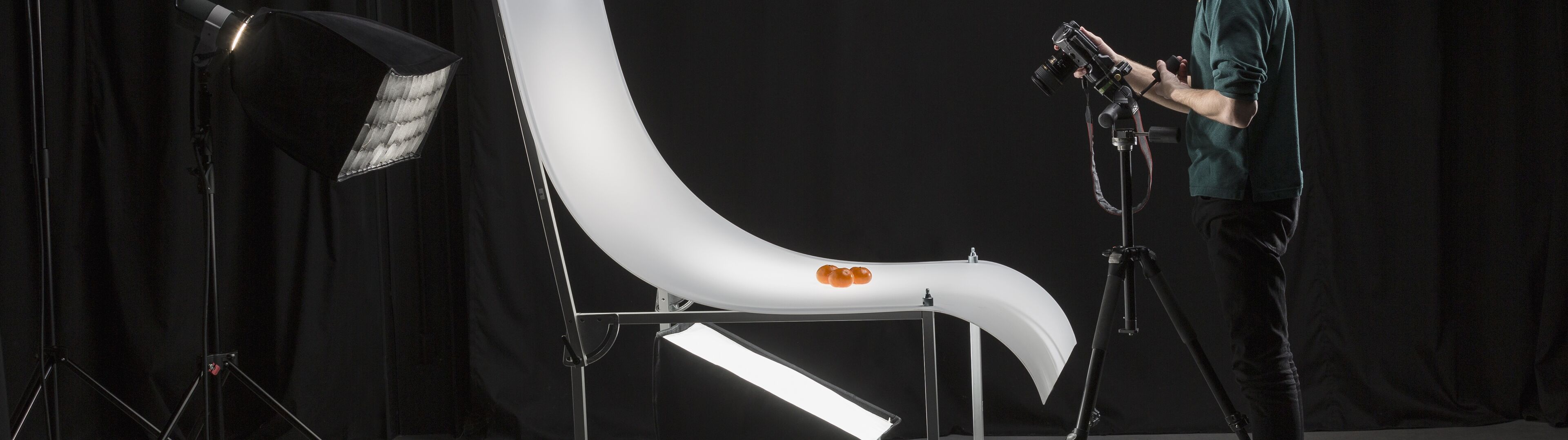 A photographer adjusting equipment in a professional studio for product photography, with lighting and a white backdrop.